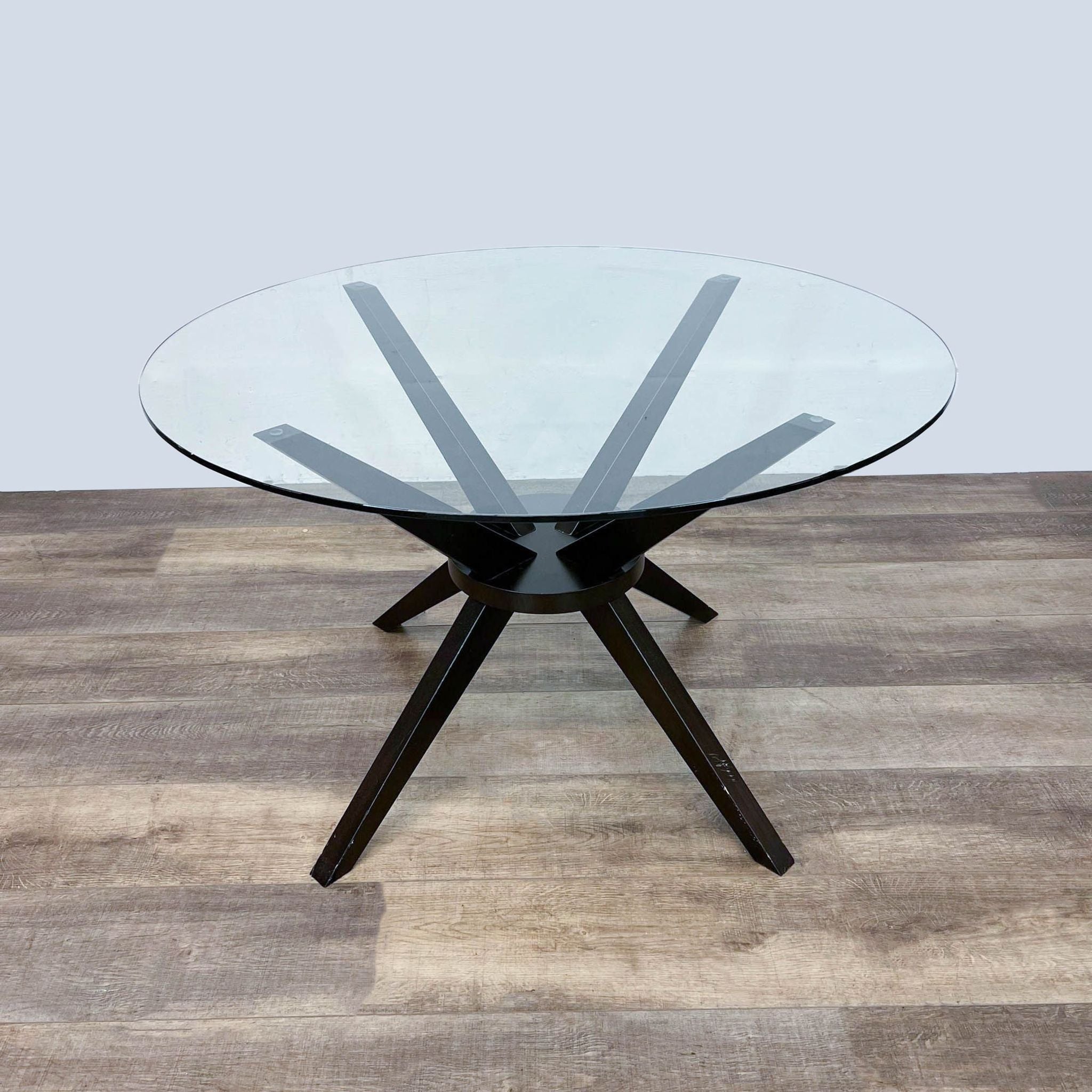 Reperch brand contemporary modern round dining table with angular solid wood dark legs and a clear tempered glass top.