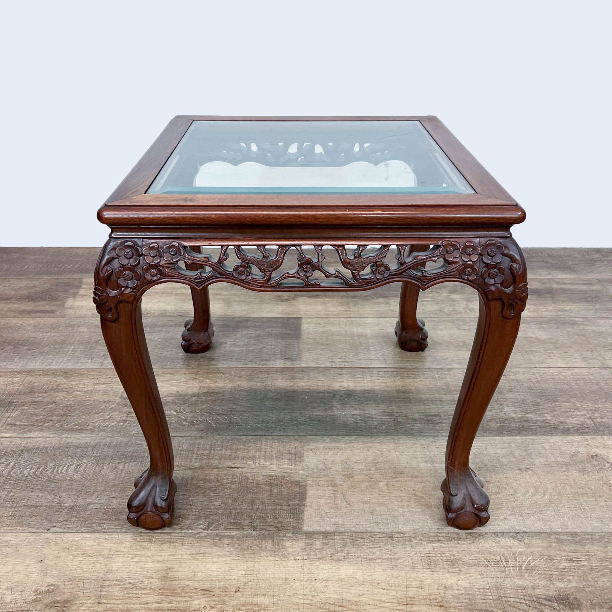 Reperch Chinese Chippendale end table with intricate carving and glass top, showing ball and claw feet on wooden floor.