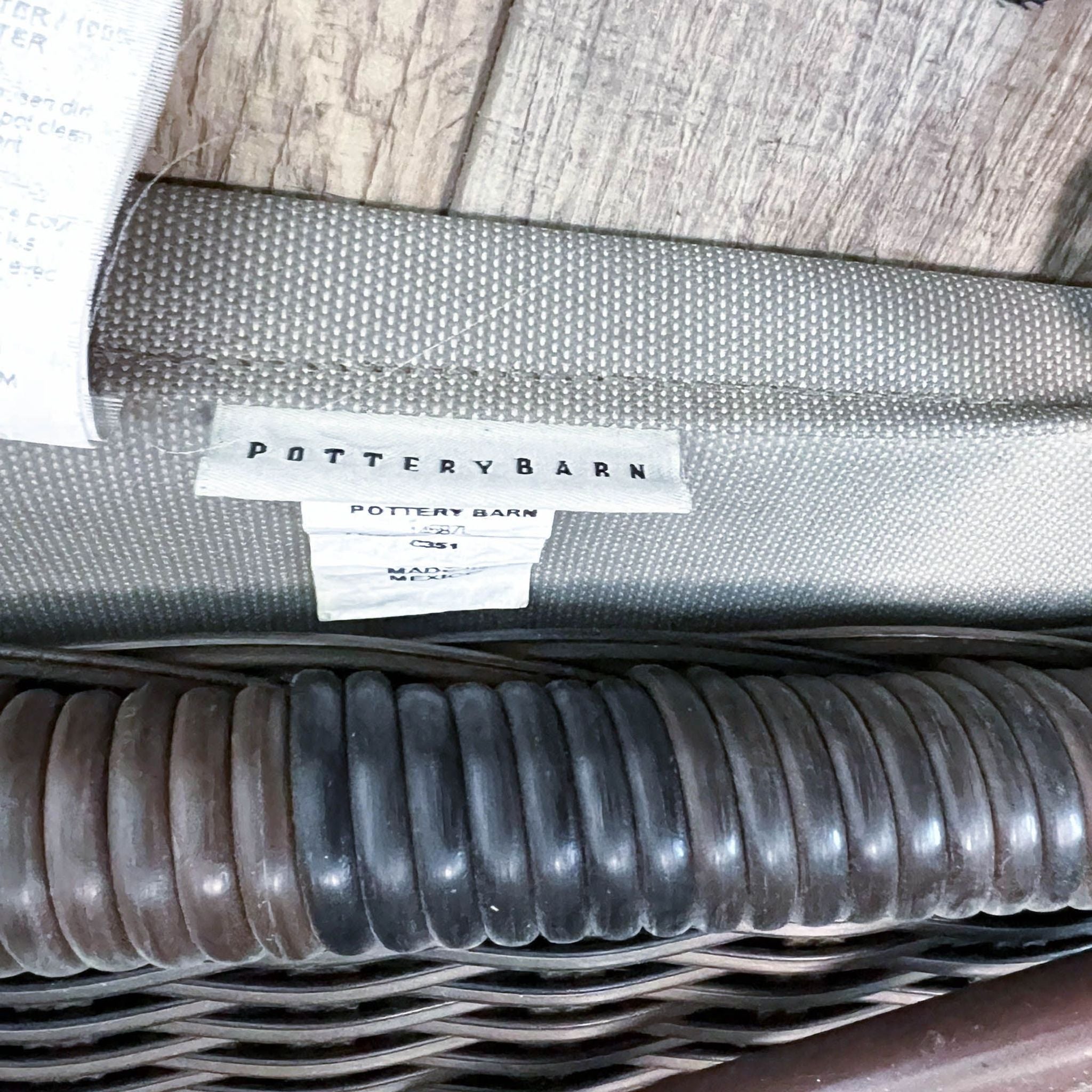 Close-up of a protective cover and brand tag on a hand-woven resin wicker double chaise by Pottery Barn, displaying texture and branding detail.