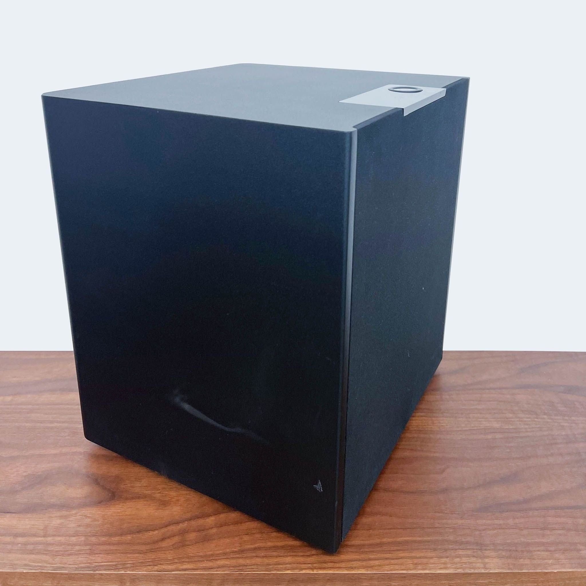 Black Triad subwoofer on wooden surface against a white background.