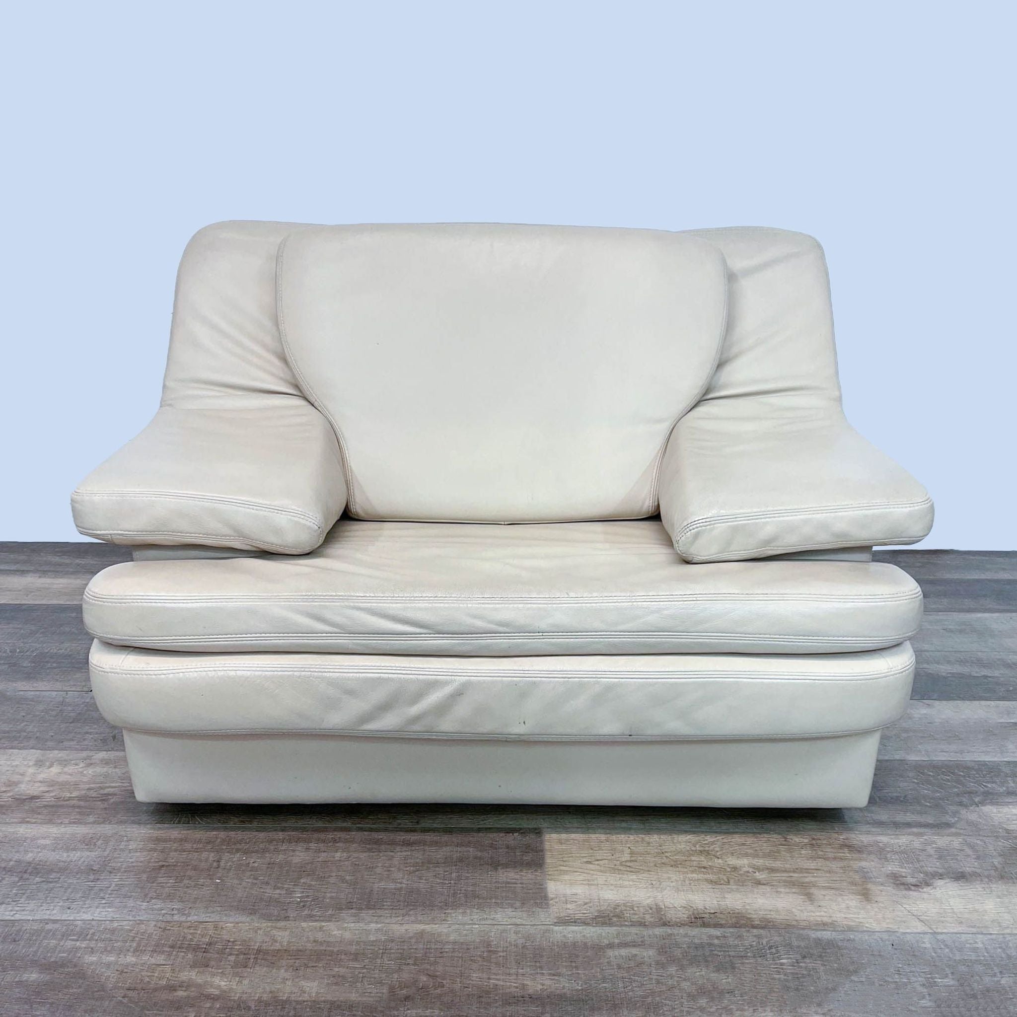 Reperch brand contemporary cream leather lounge chair with cushioning and wide armrests, set on wooden feet. Front view.