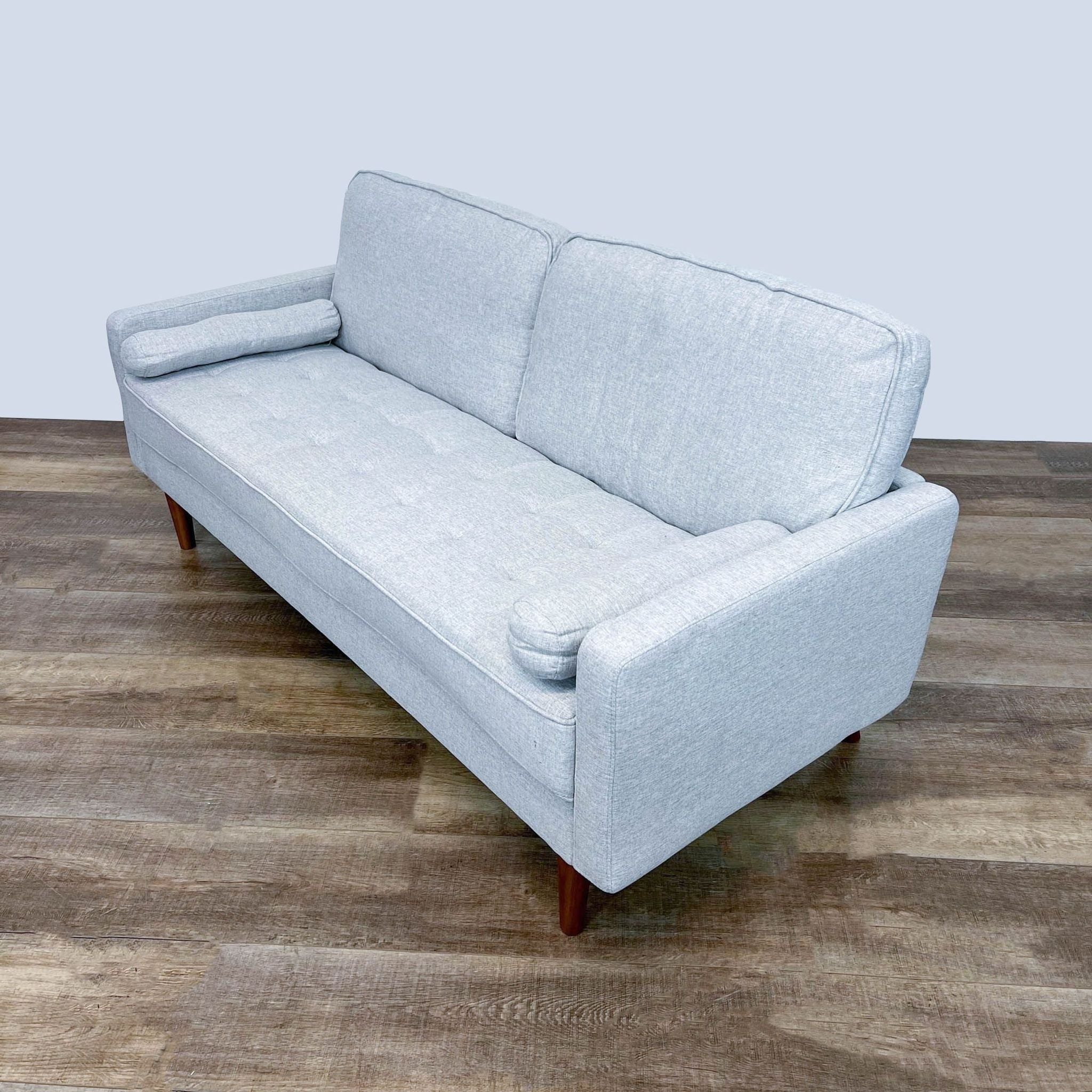 Frontal view of a narrow arm Reperch loveseat with wood finish feet and bolster cushions on a wooden floor.