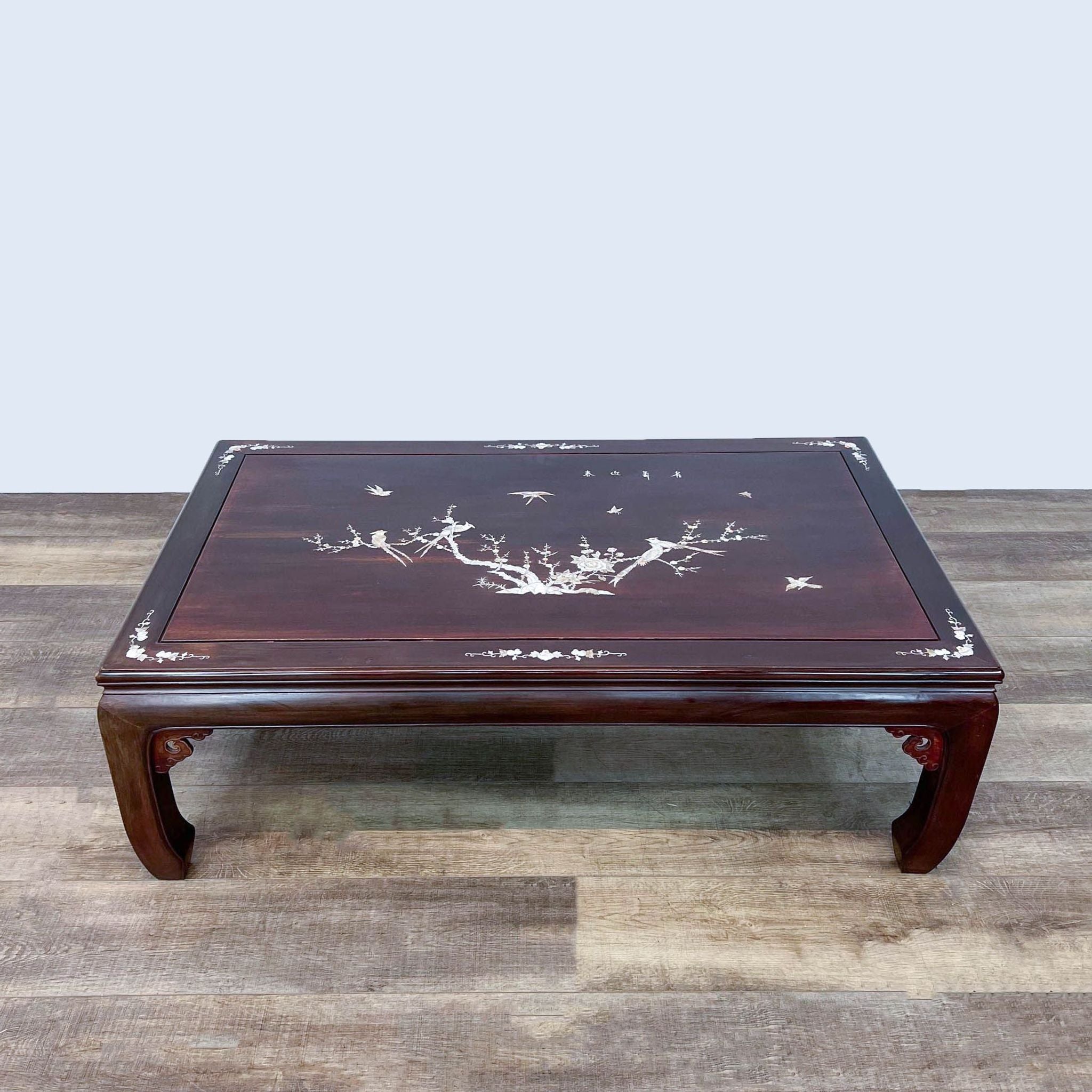 Dark wooden Reperch coffee table featuring intricate mother of pearl inlay design, positioned on a wooden floor.