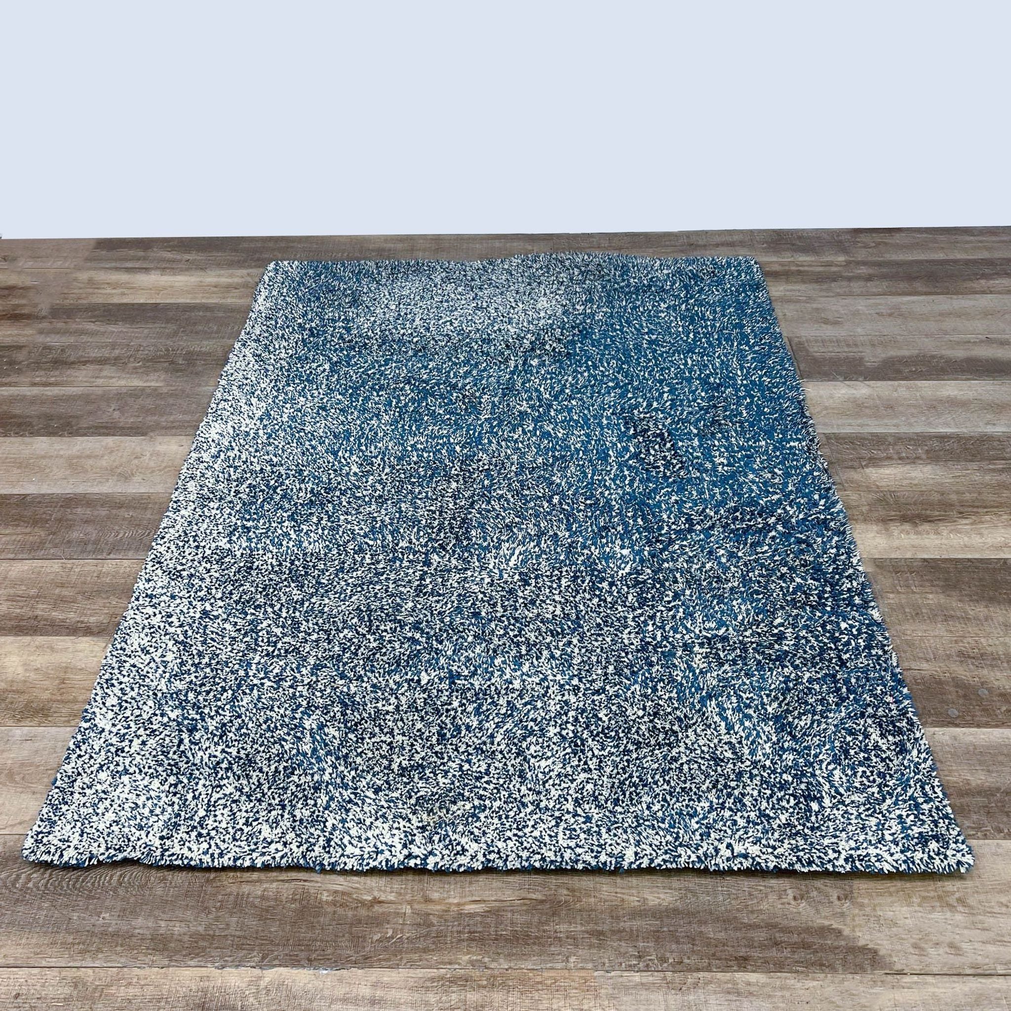 KAS Bliss 5'x7' area rug on wooden floor, showcasing its stain-resistant 1" polyester pile in shades of blue and white.