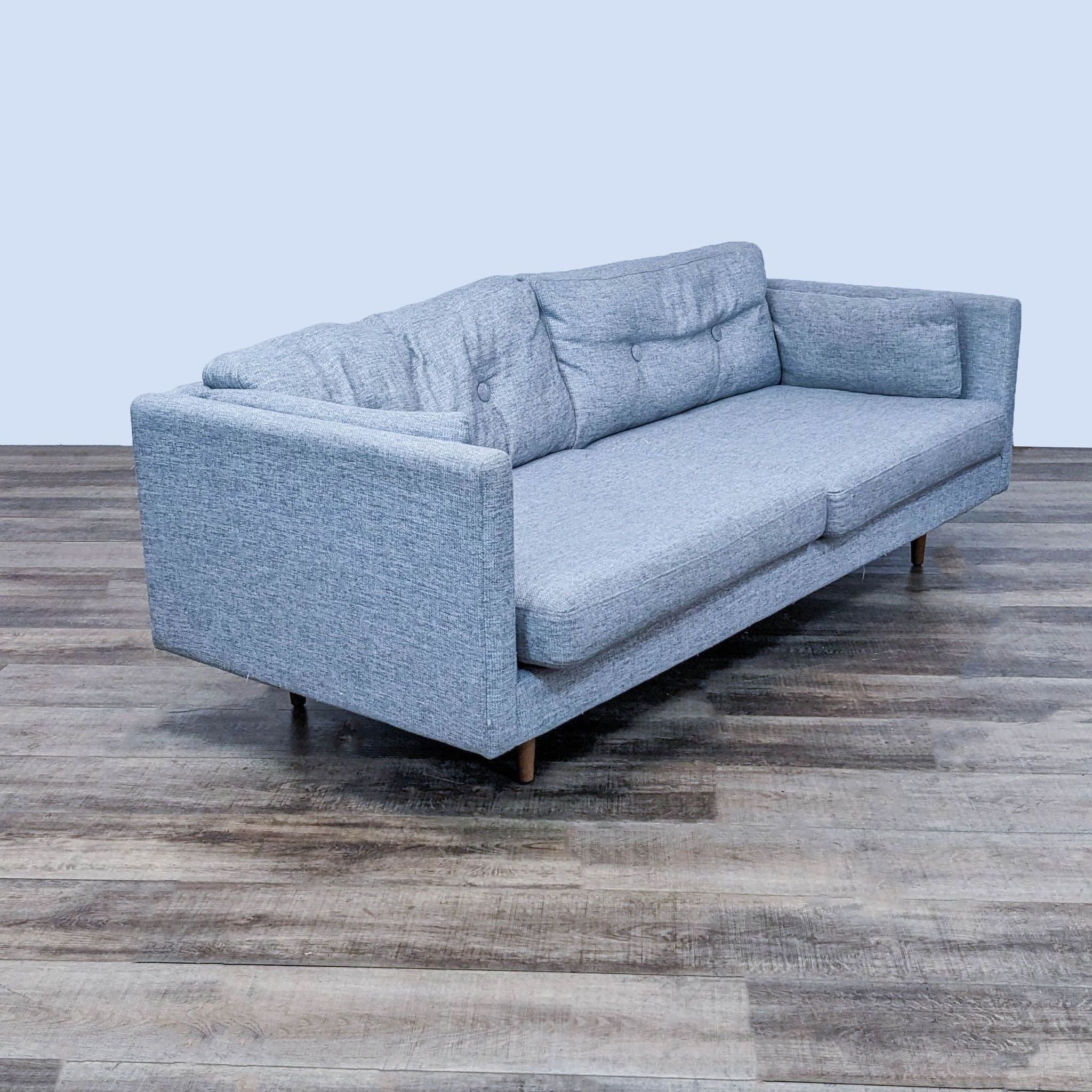 Alt text 2: An angled perspective of a gray 3-seat fabric sofa by Article with button-tufted backrest, two side accent pillows, narrow arms, and wooden walnut finished legs.