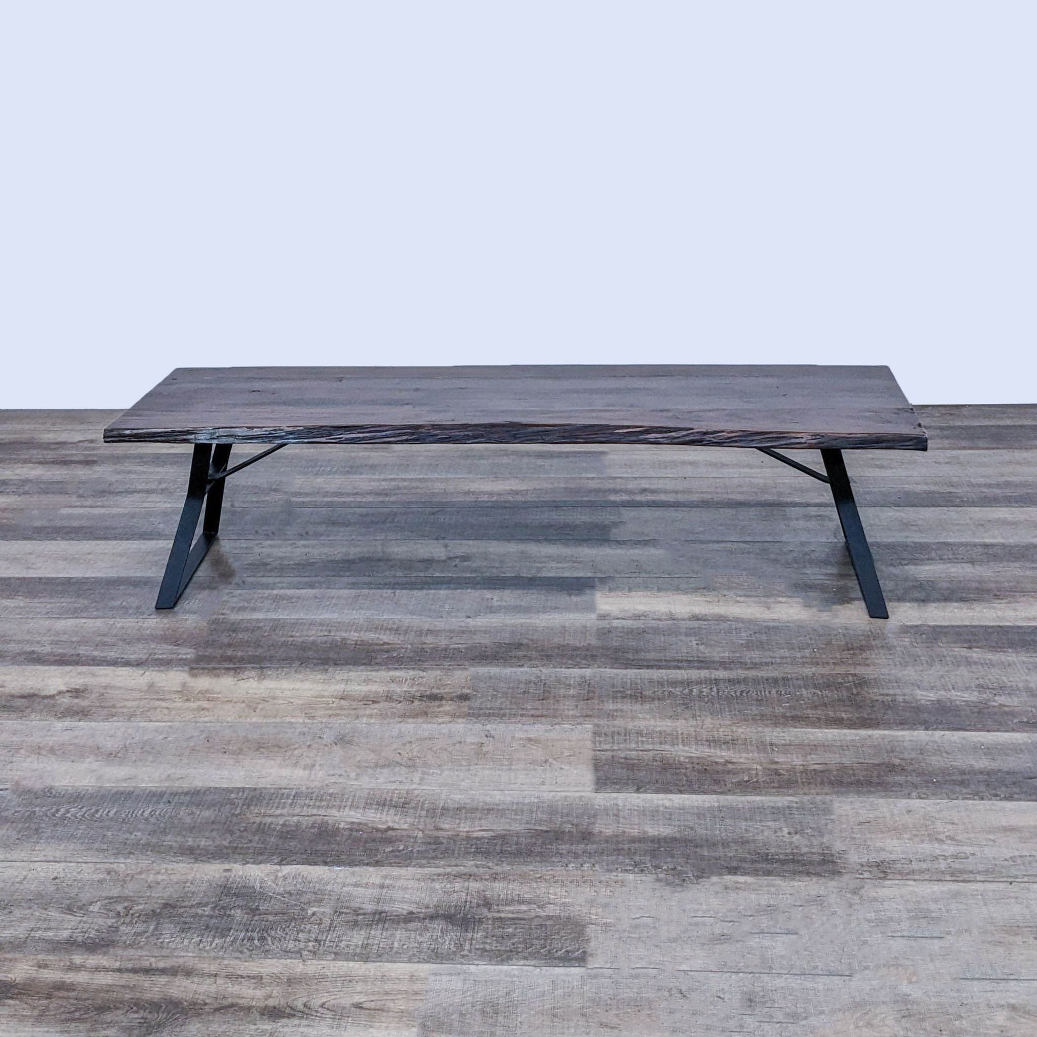 Dark-toned Reperch coffee table with a sleek metal base, positioned on a textured wood floor.