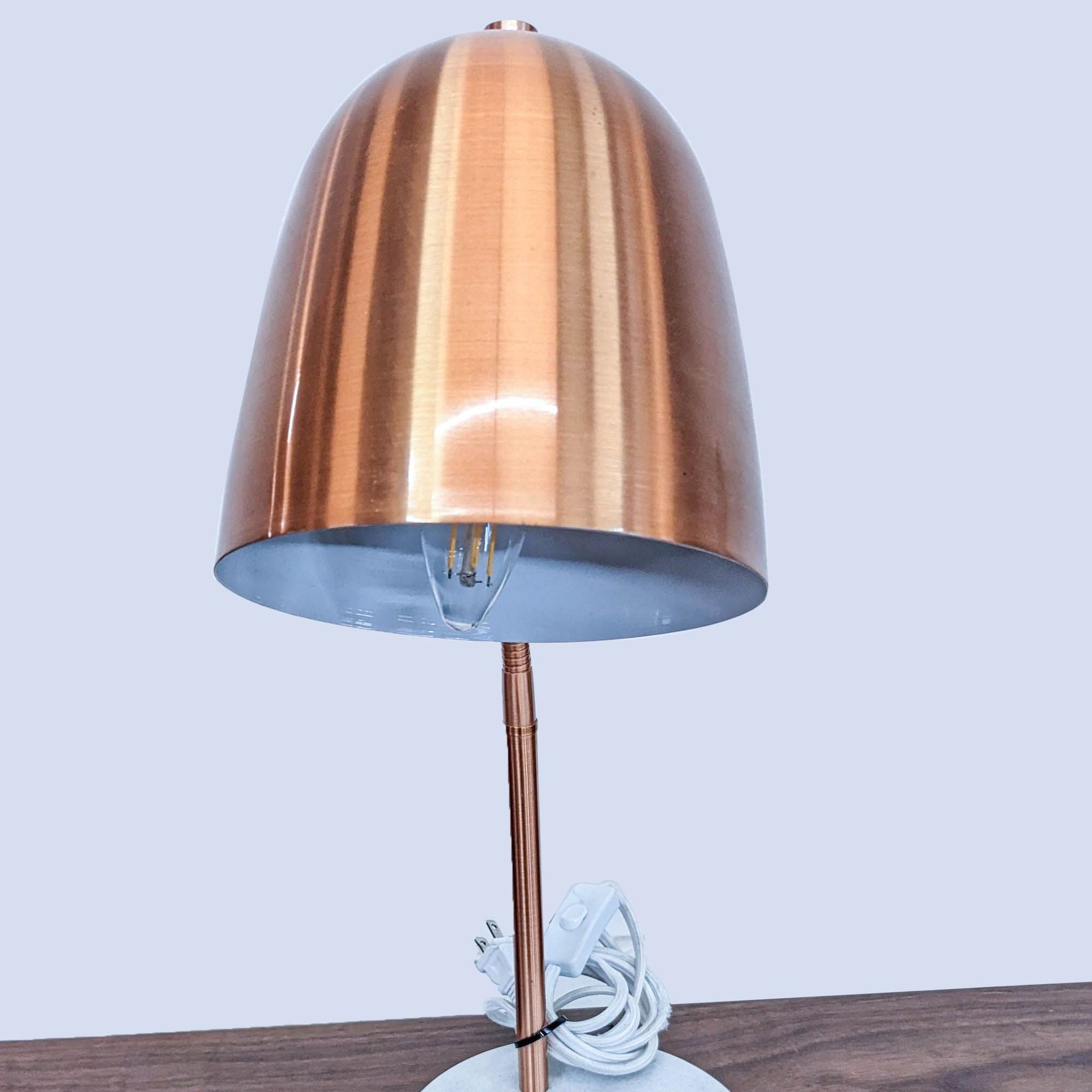 Reperch desk lamp with an arched copper stand and visible bulb, marble base on wood surface.
