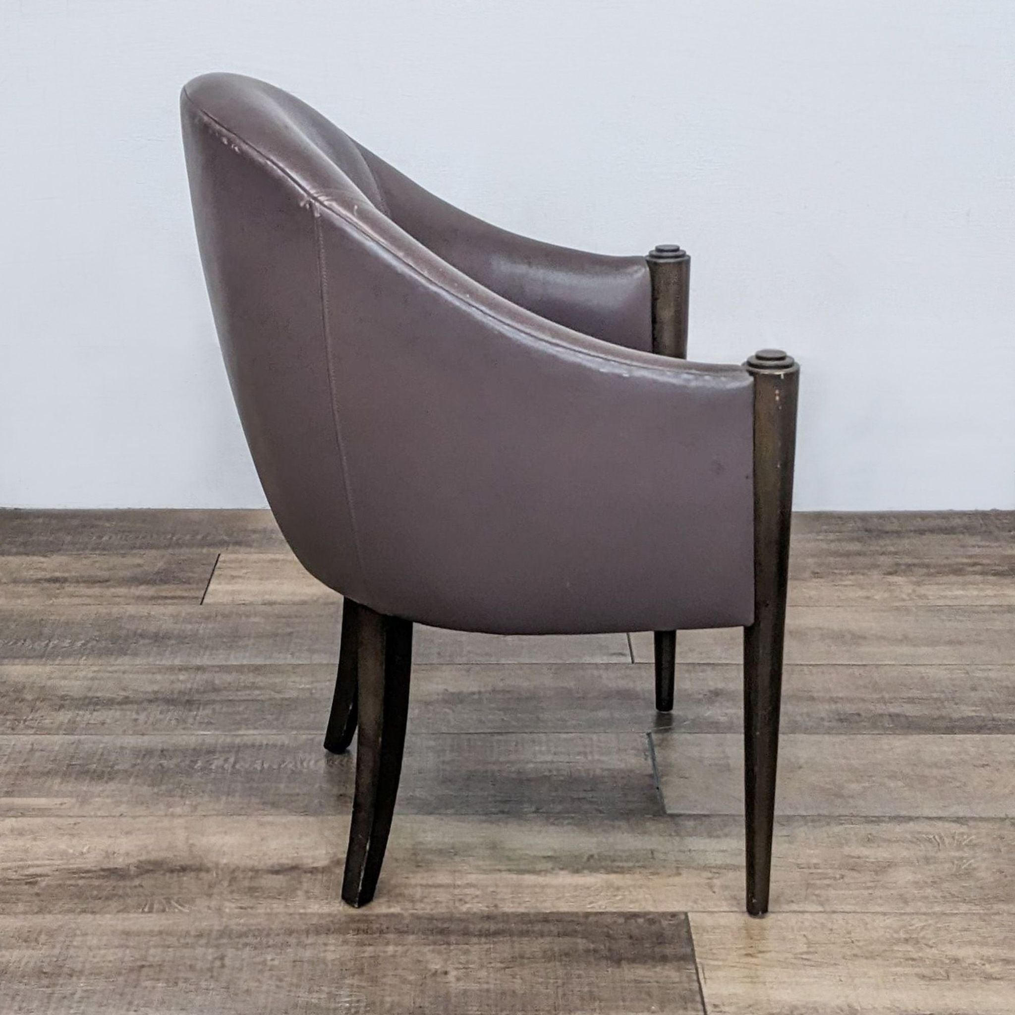 Side view of a Donghia leather lounge chair showcasing its curved back design and step down top legs on a hardwood floor.