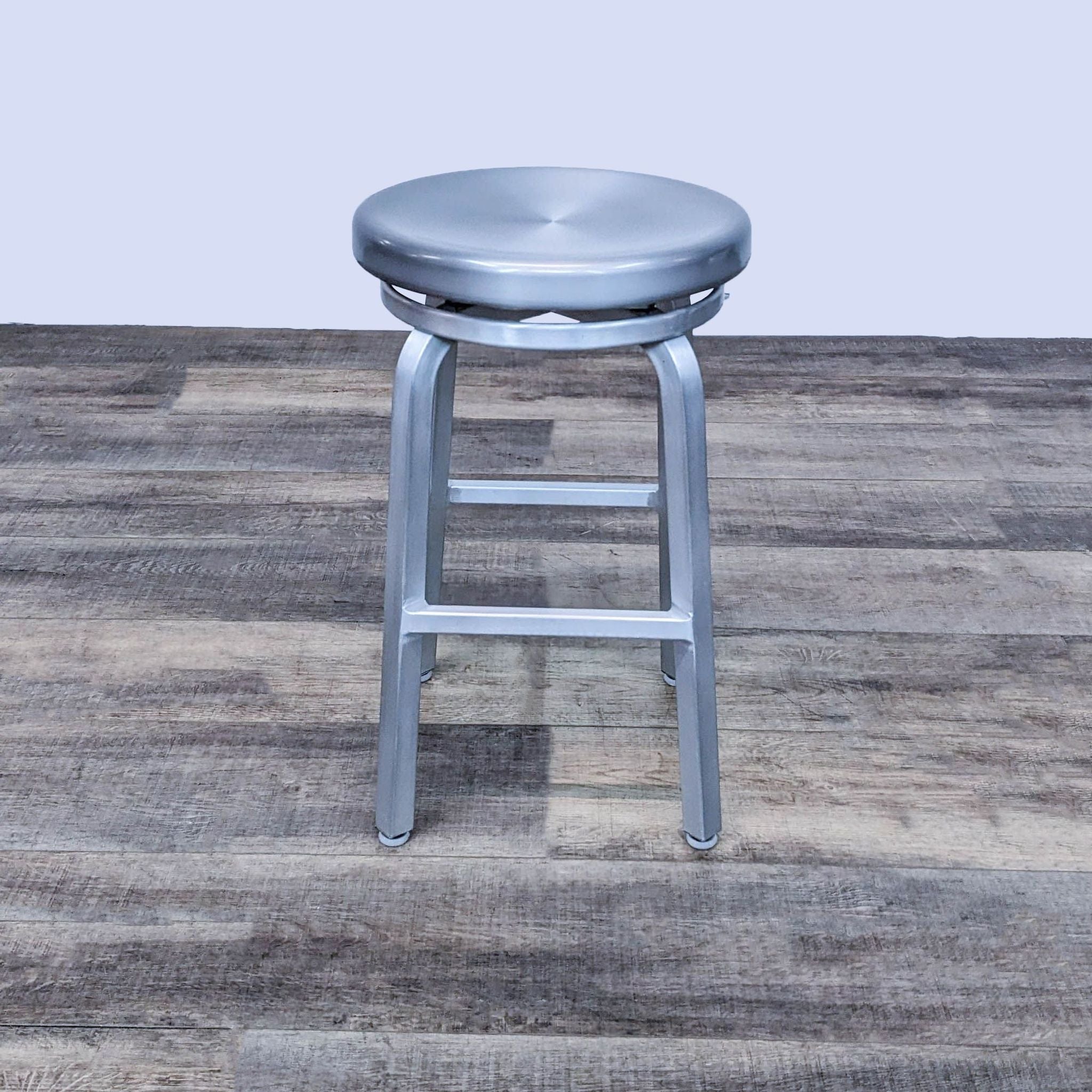 Reperch industrial-style metal stool with a round swivel seat and wooden floor background.
