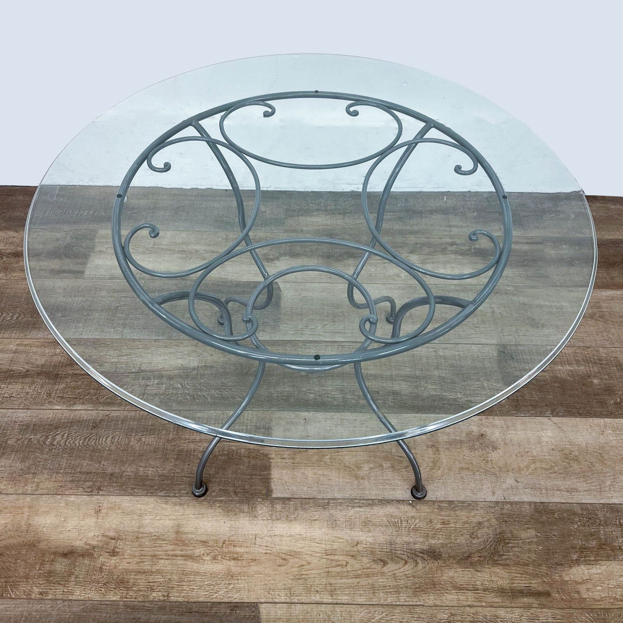 Round glass Reperch dining table with ornate powder-coated metal base, top view on a wooden floor.