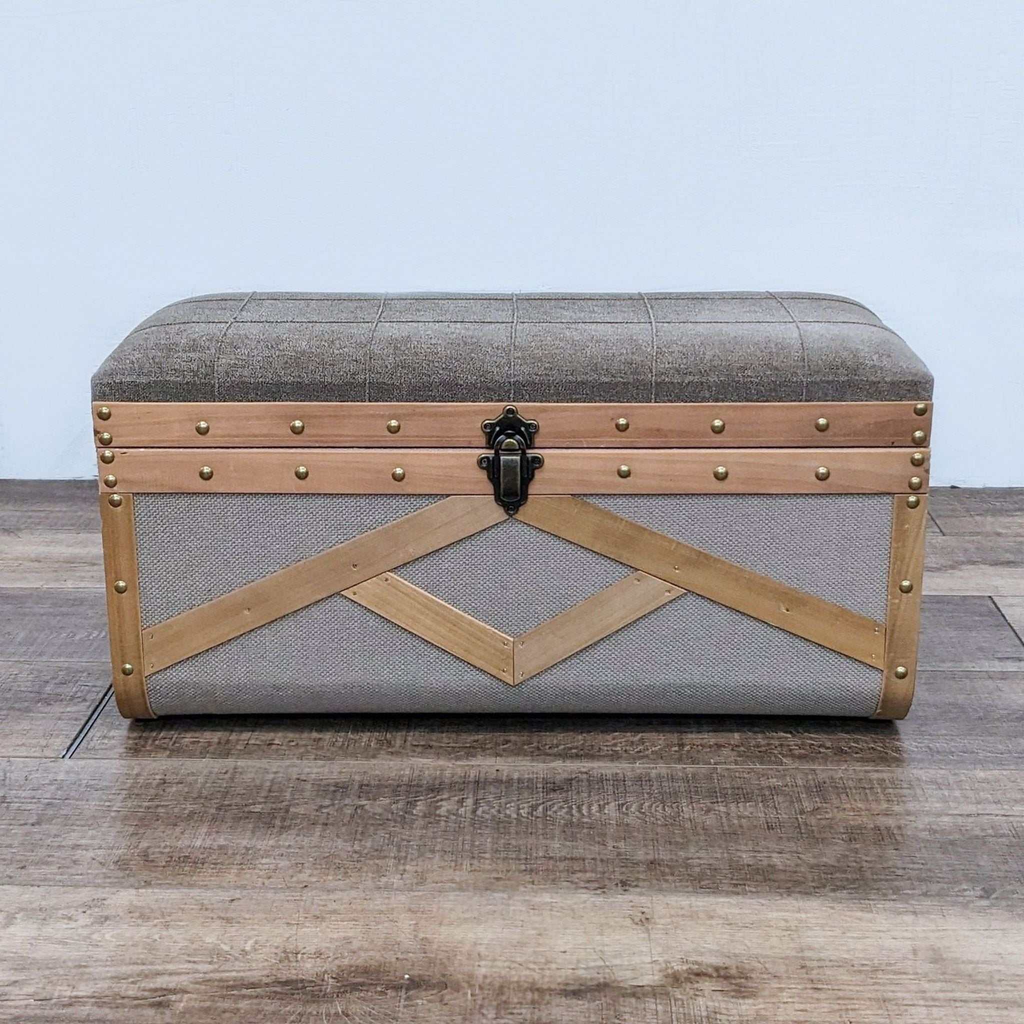 Reperch fabric trunk with wood detailing and brass nail studs, closed, on wooden floor.