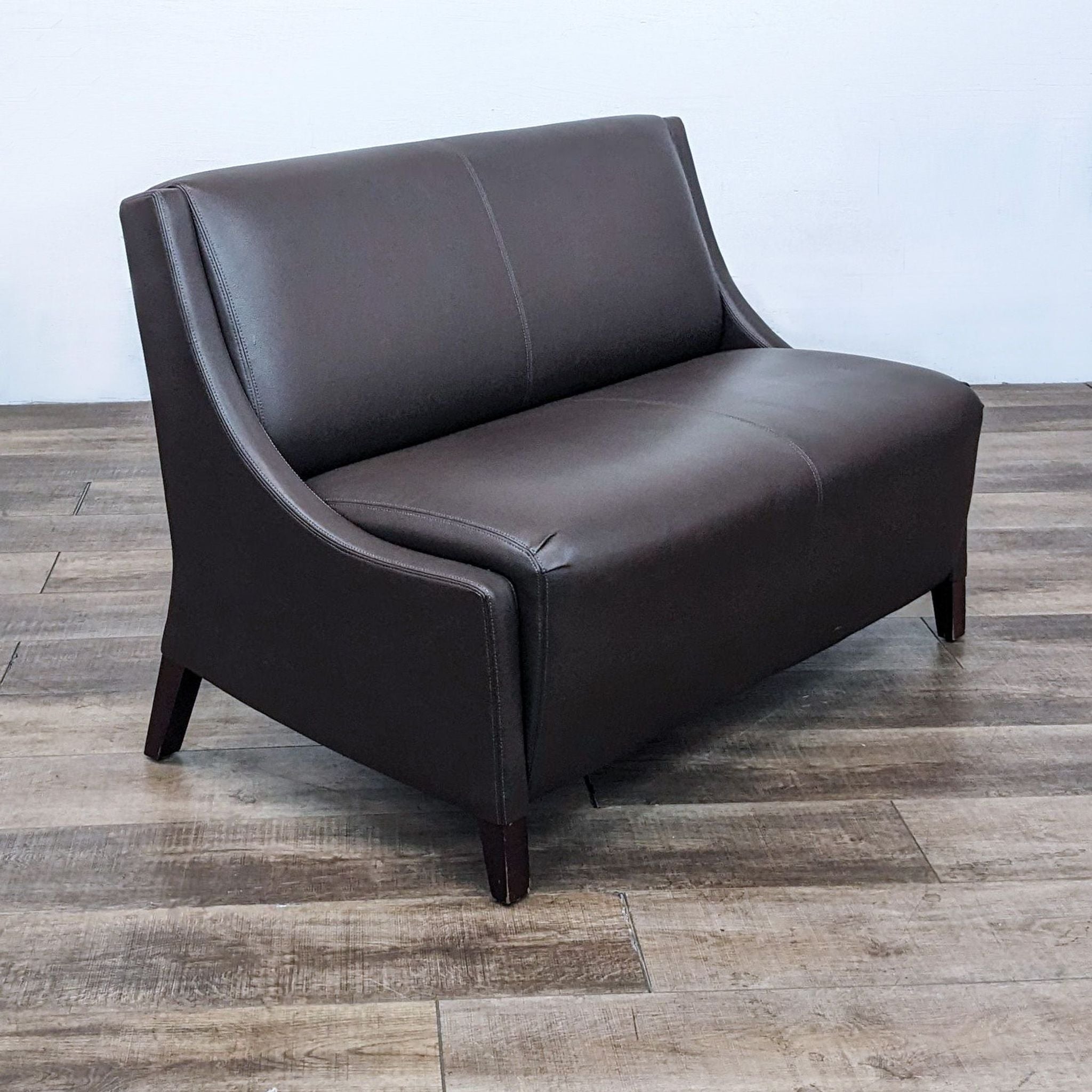 Brown Reperch 78" loveseat showing a close-up of the leather texture and stitching details on a wooden floor backdrop.