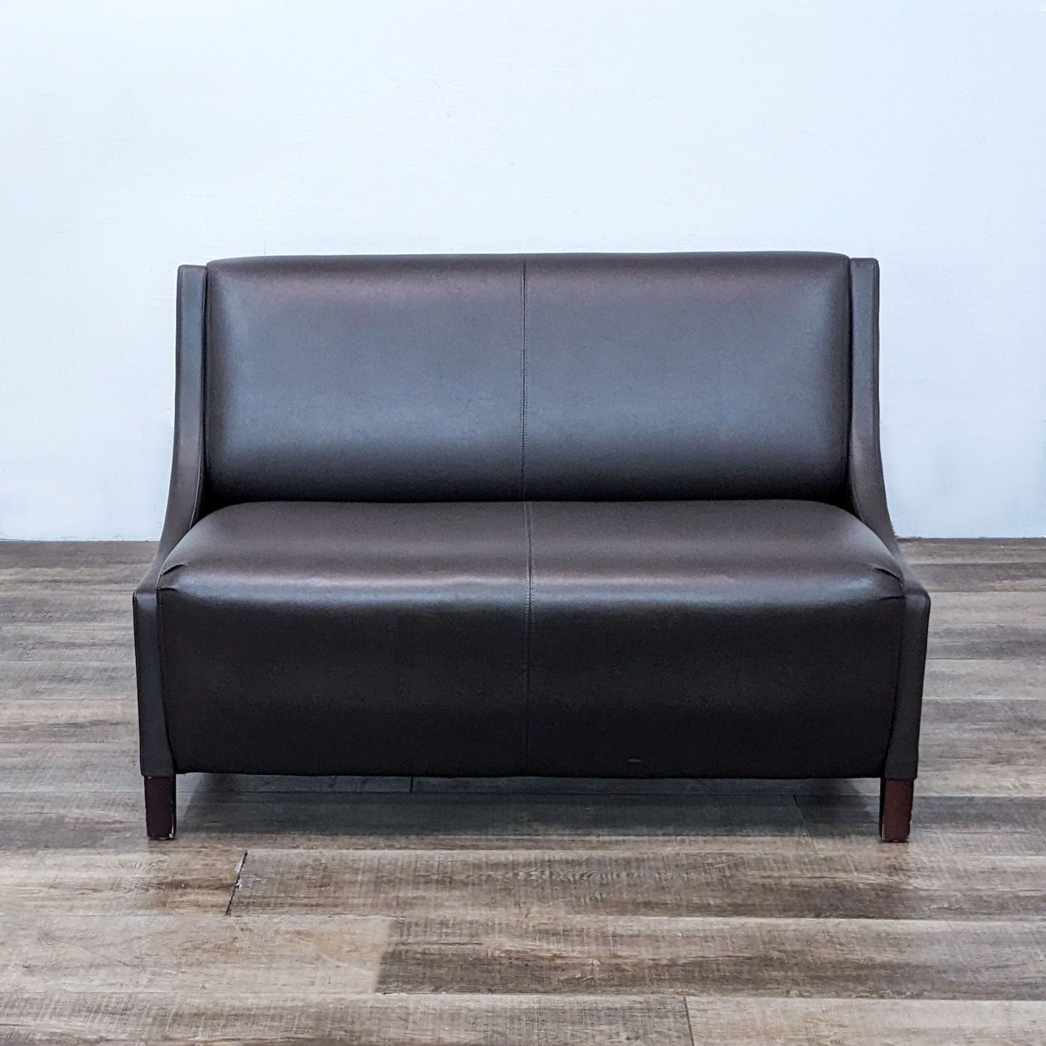 Reperch brown leather-look loveseat with clean lines and dark wood feet, positioned on a wooden floor.
