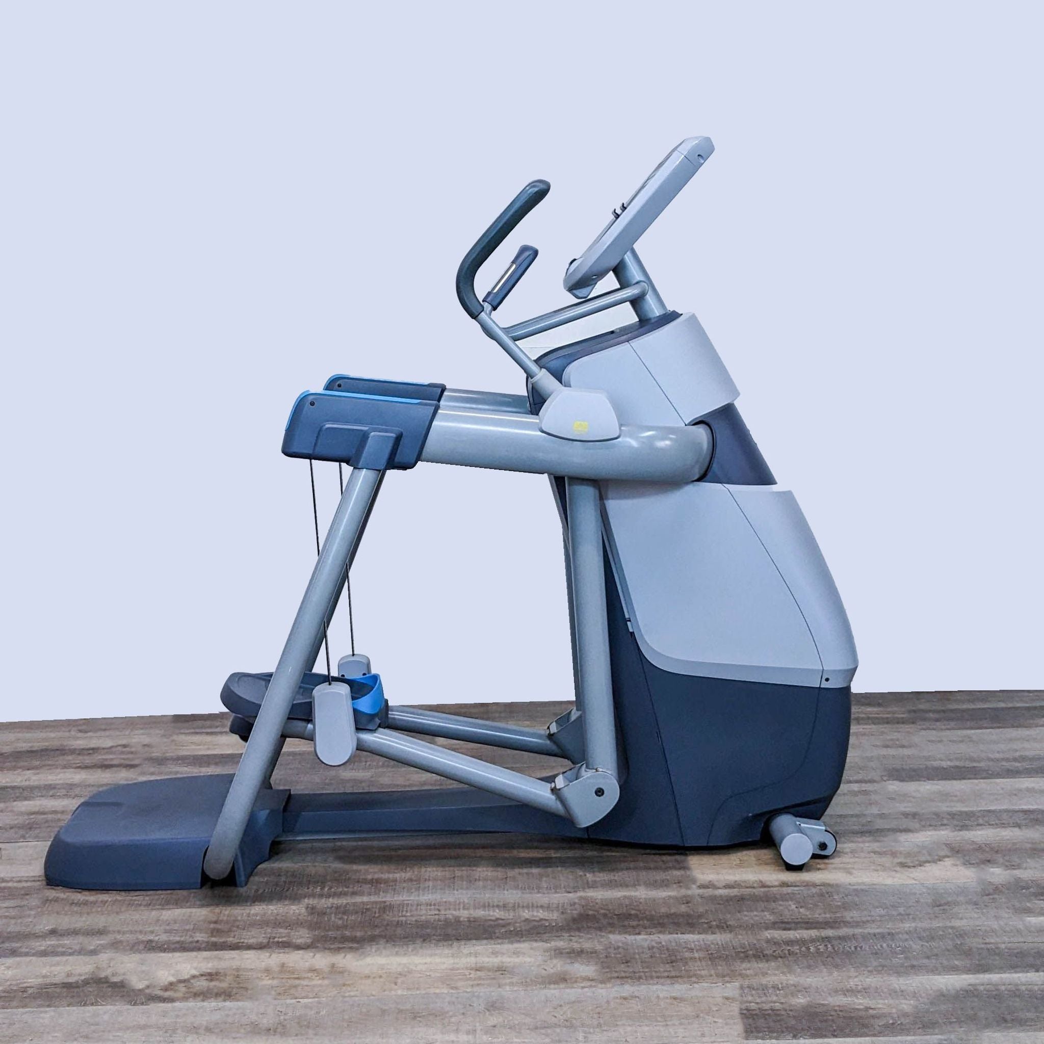 Rear view of a Precor elliptical machine showing the stride mechanism and wheels on a wooden floor.