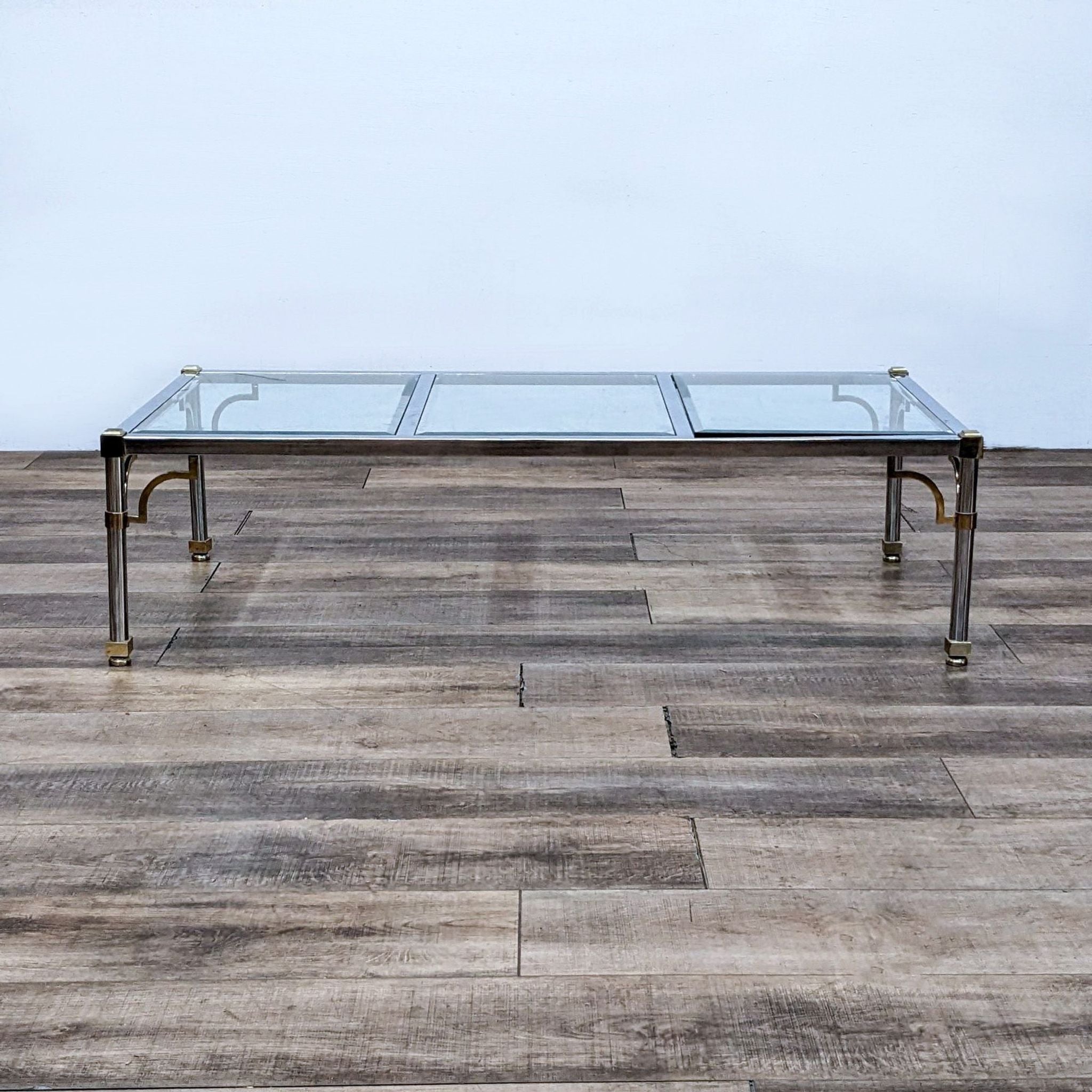 Rectangular Reperch coffee table with glass top and gold accents on legs against wooden floor.