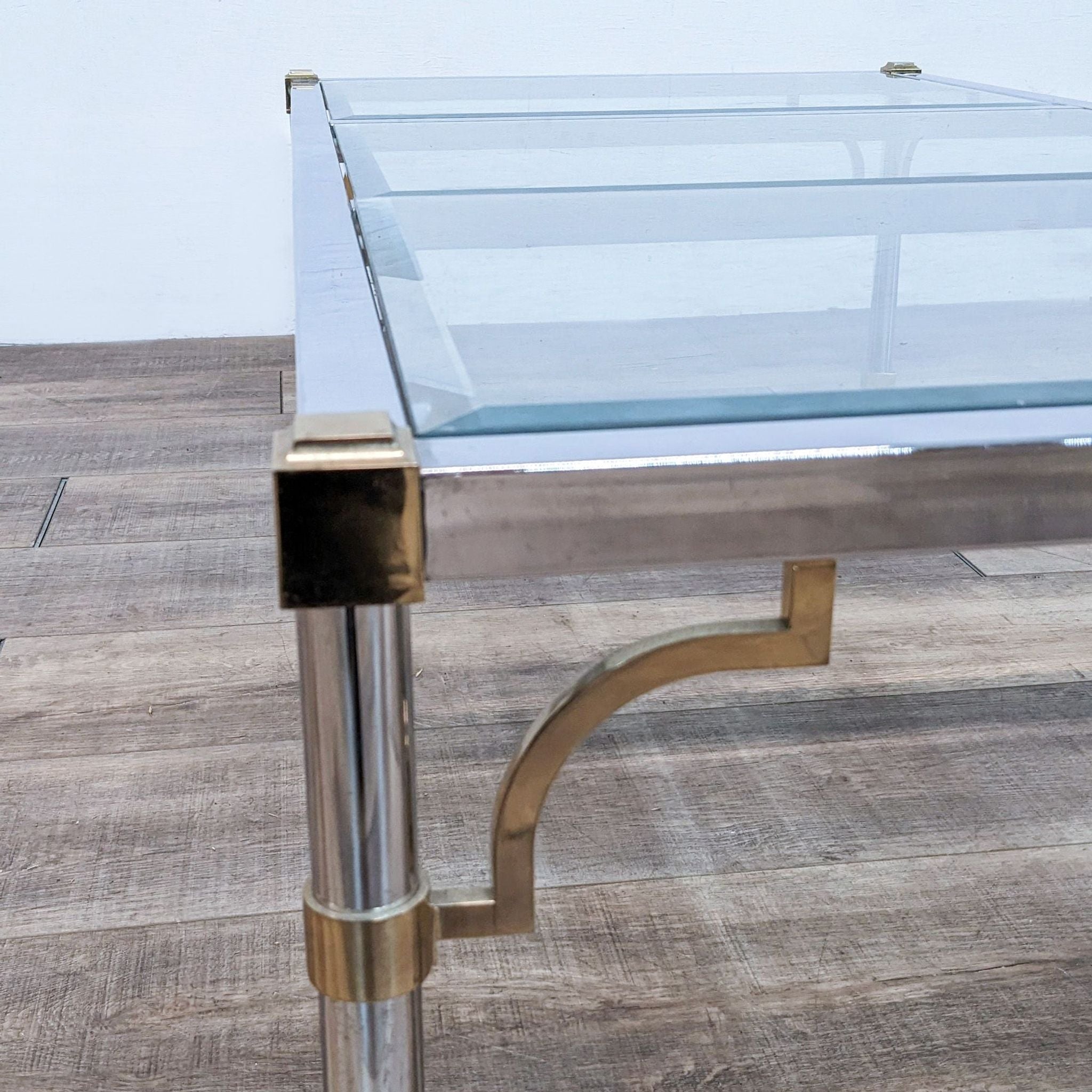 Reperch brand coffee table with a clear glass top and polished metallic legs on a wooden floor.
