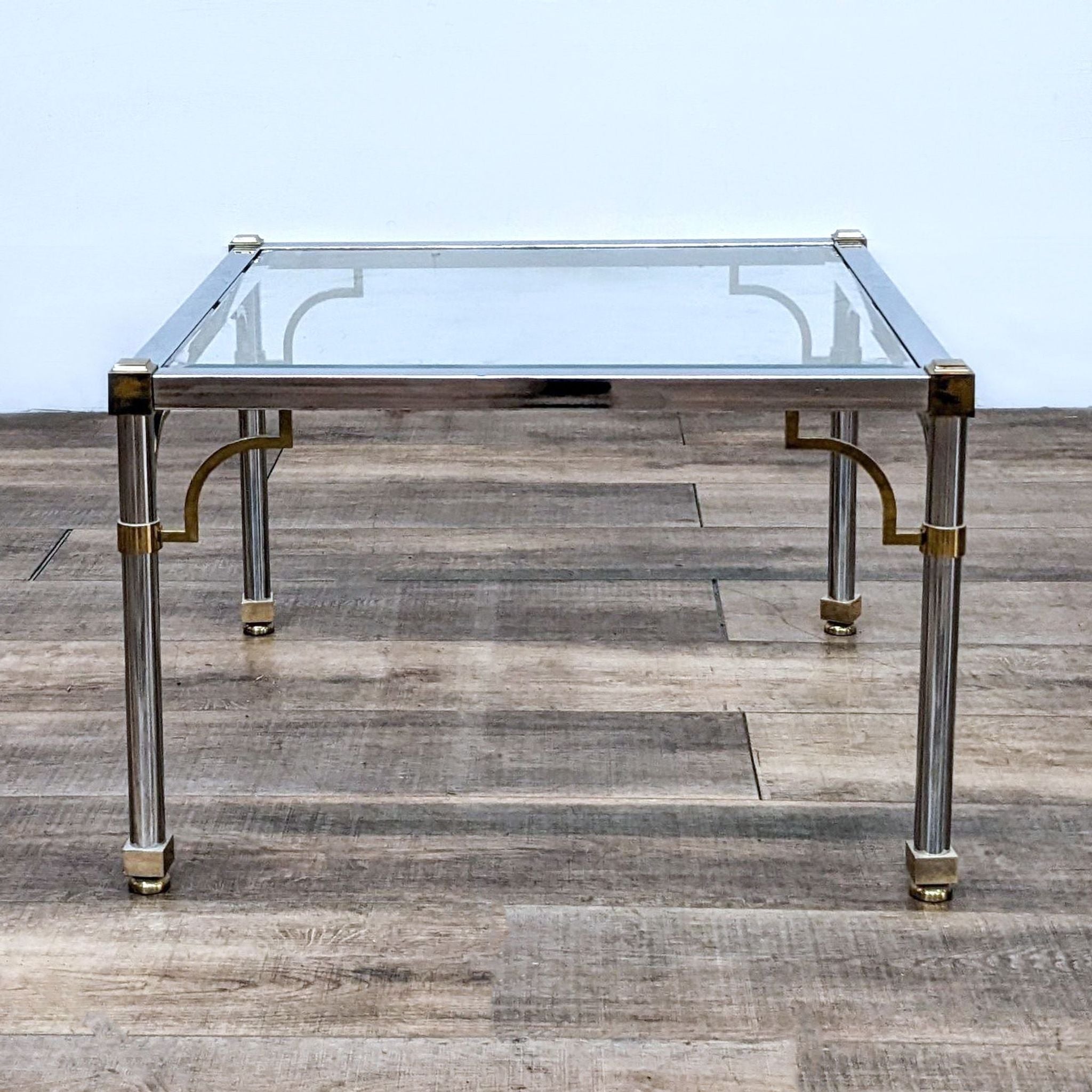 Reperch brand end table with a clear glass top and gold-tone metal legs on a wooden floor.