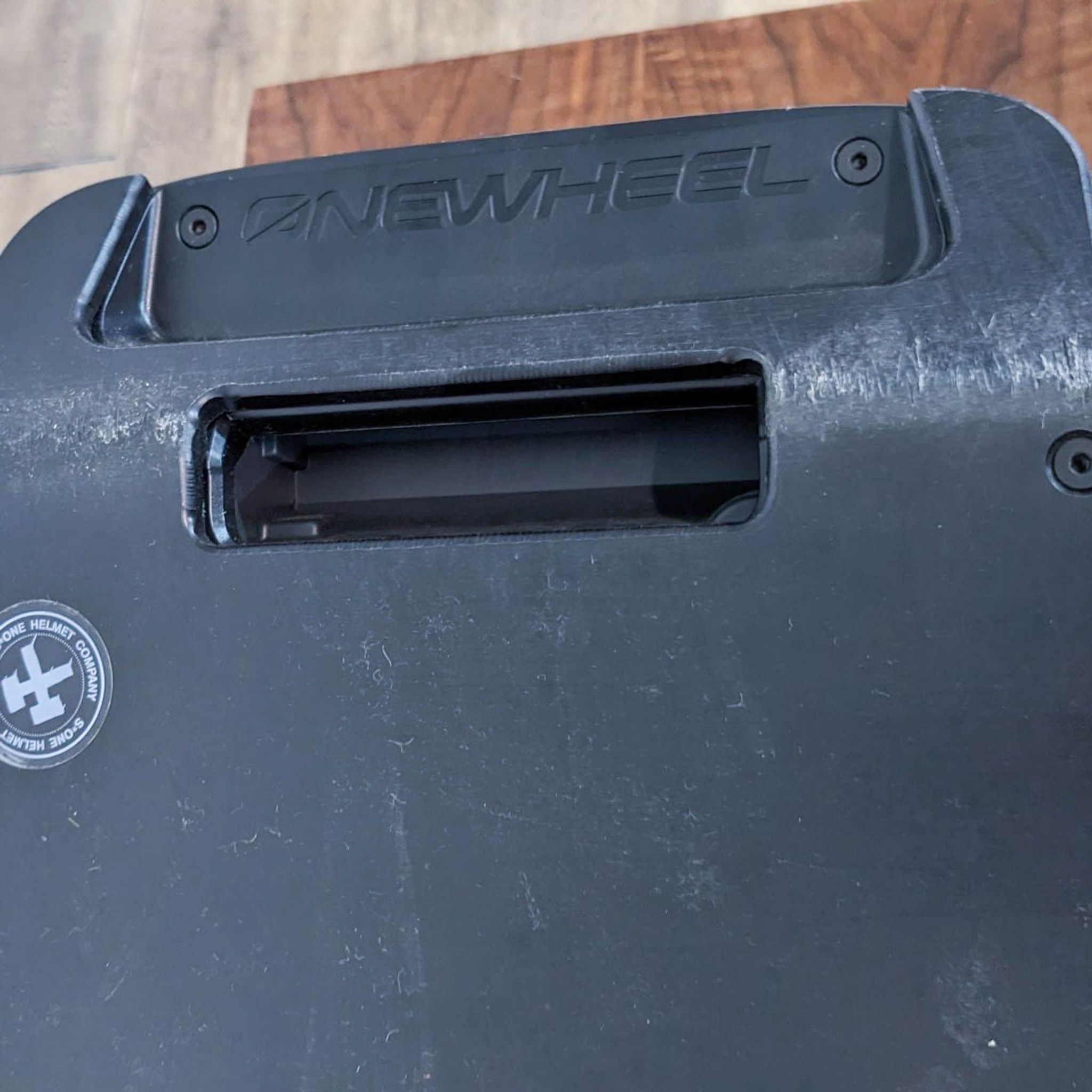 Rear view of an electric skateboard featuring the Onewheel logo and a handle slot on its black fender.