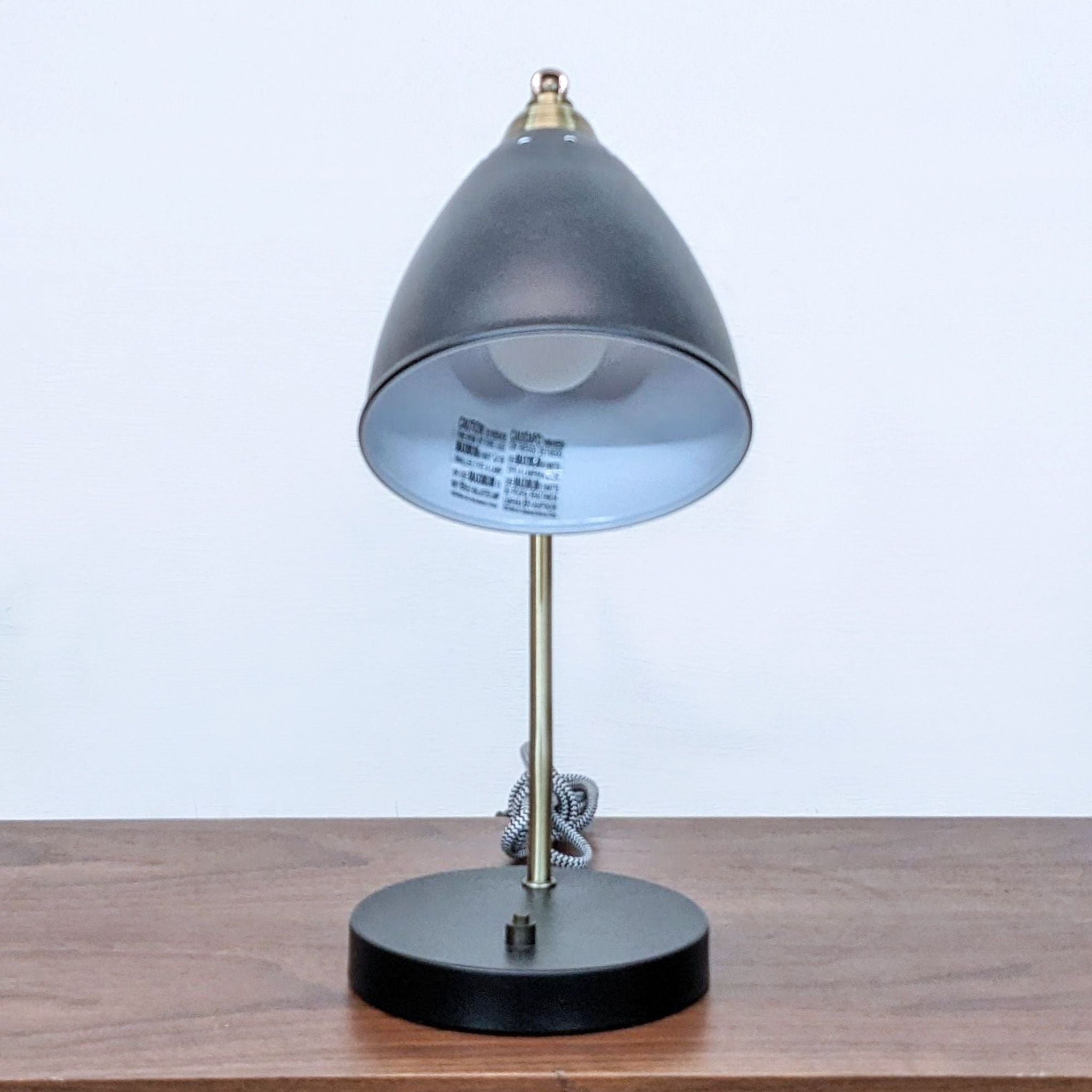 Reperch brand desk lamp with angled brass stand and gray shade, illuminated interior visible, on a wooden surface.