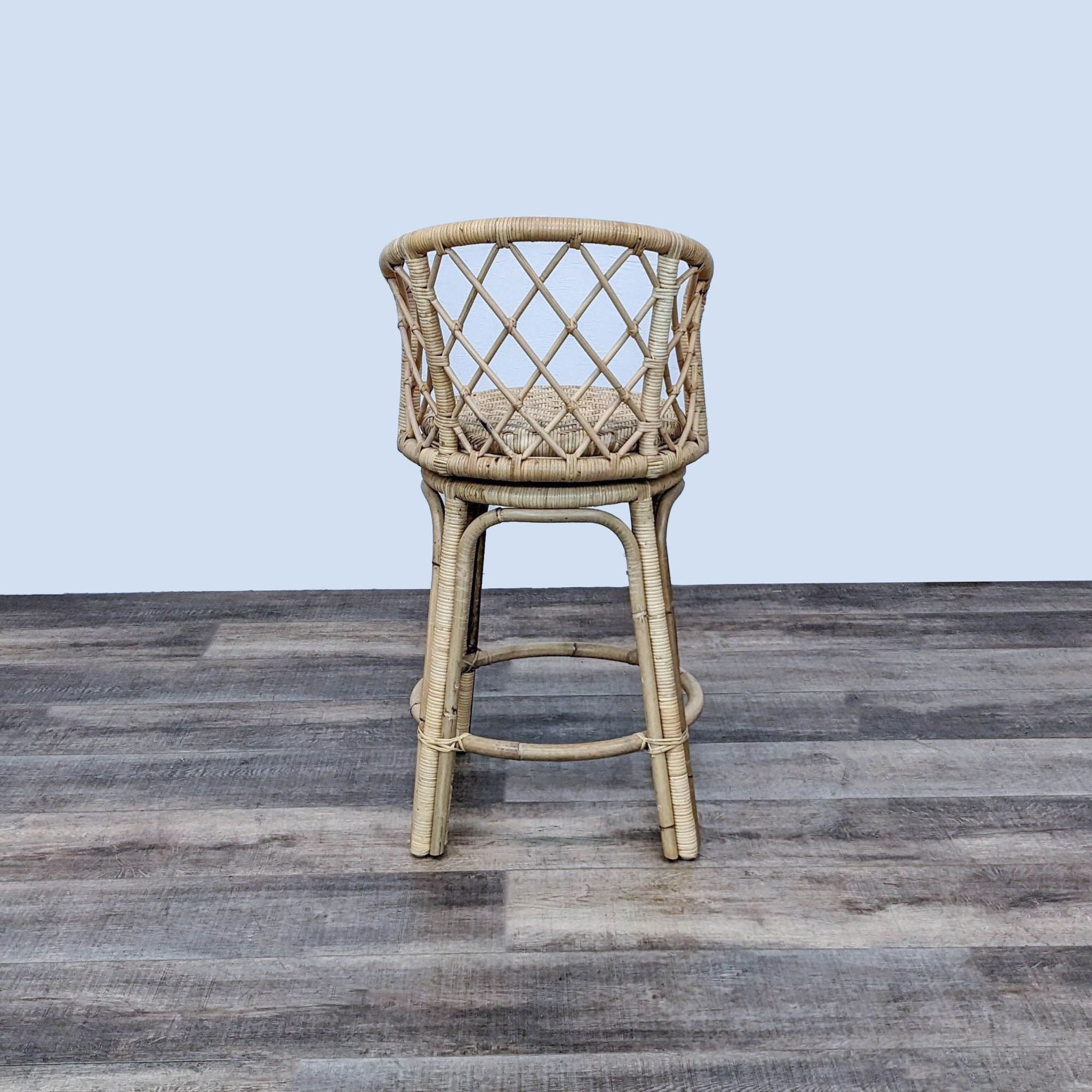 Serena and Lily Avalon rattan swivel stool in natural color with open weave criss-cross back on a wooden floor.