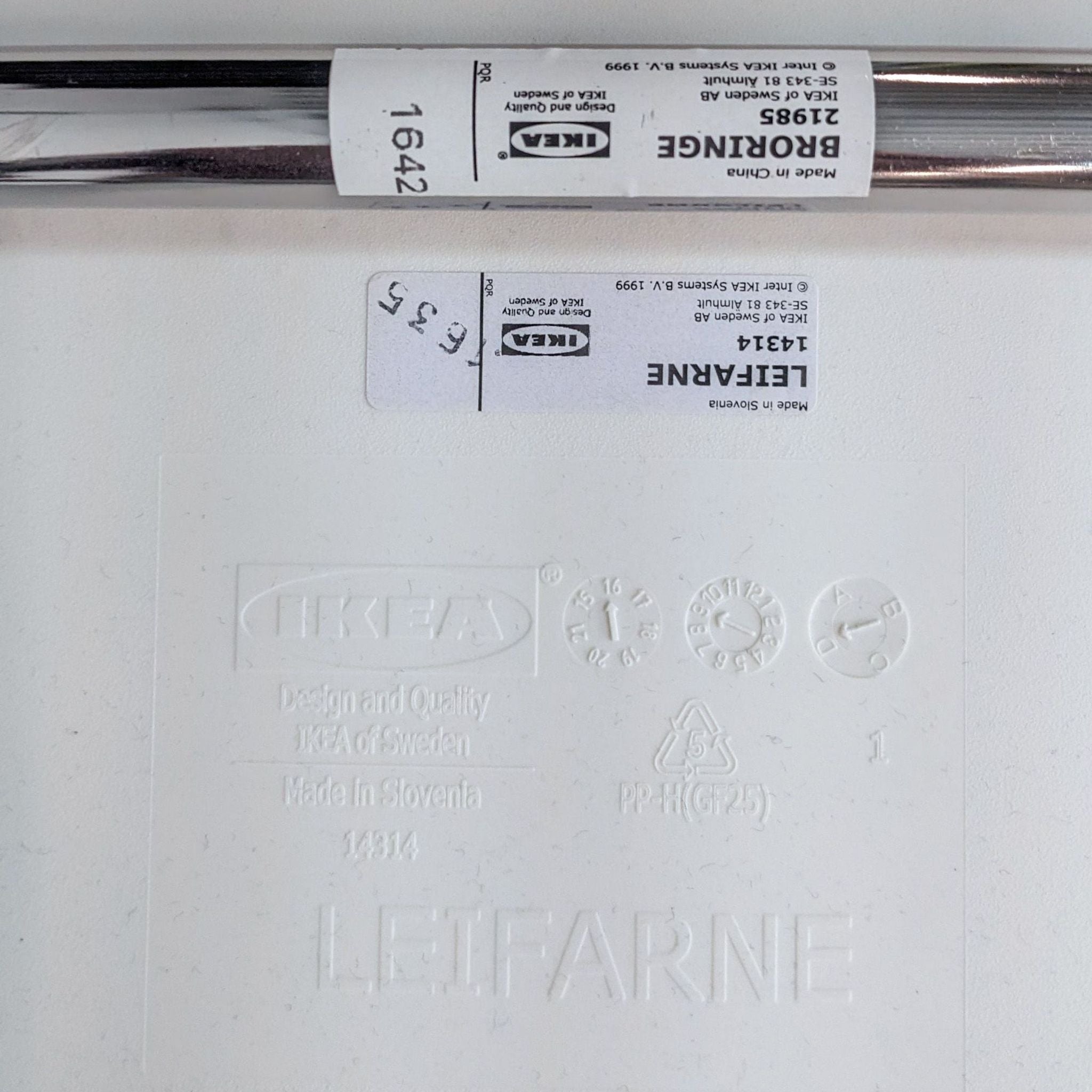 Close-up of the embossed IKEA branding and specifications on the white ergonomic polypropylene seat of the Broringe side chair with metal chrome base.