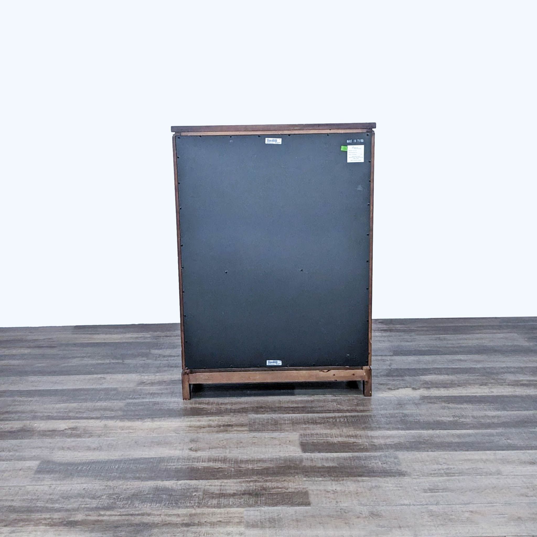 Rear view of a Reperch contemporary chest of drawers with a black backing, on a wood floor.