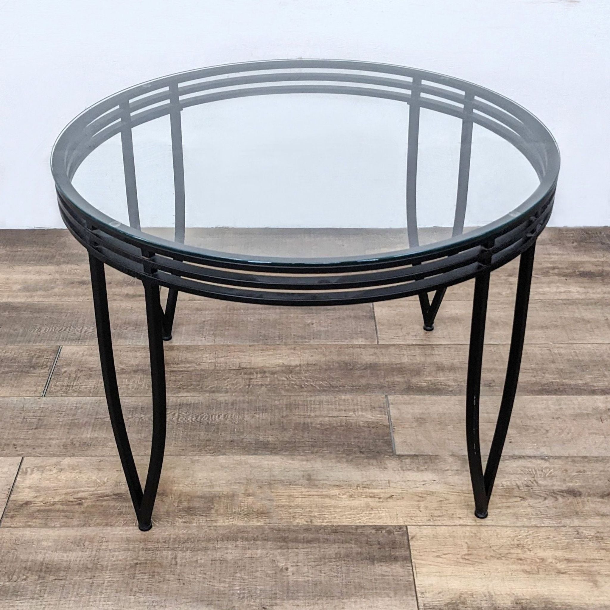 Round tempered glass-top dining table by Reperch featuring a distinctive metal base, photographed on a wooden surface.