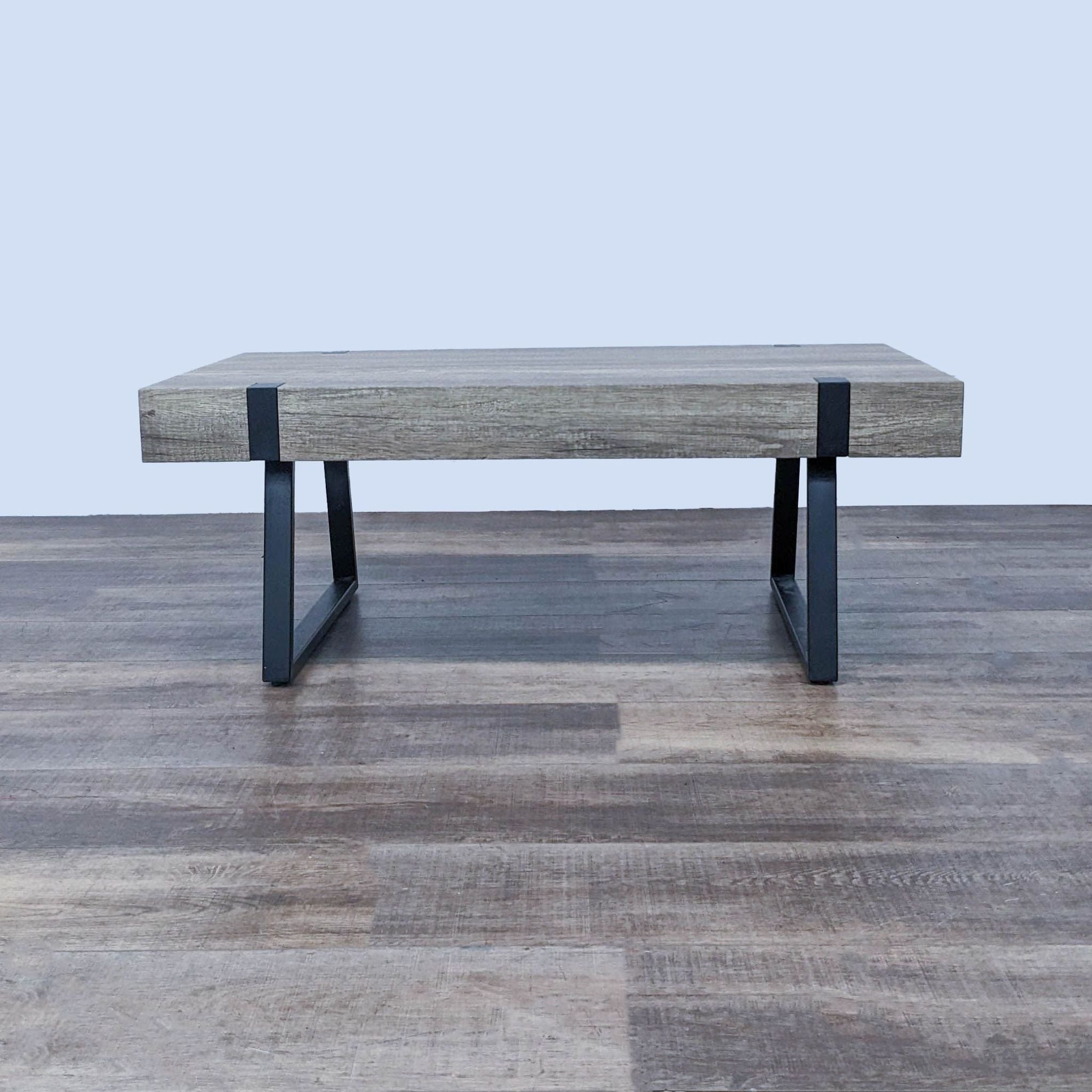 Reperch coffee table with a wooden top and black metal legs, against a wood floor and gray wall.