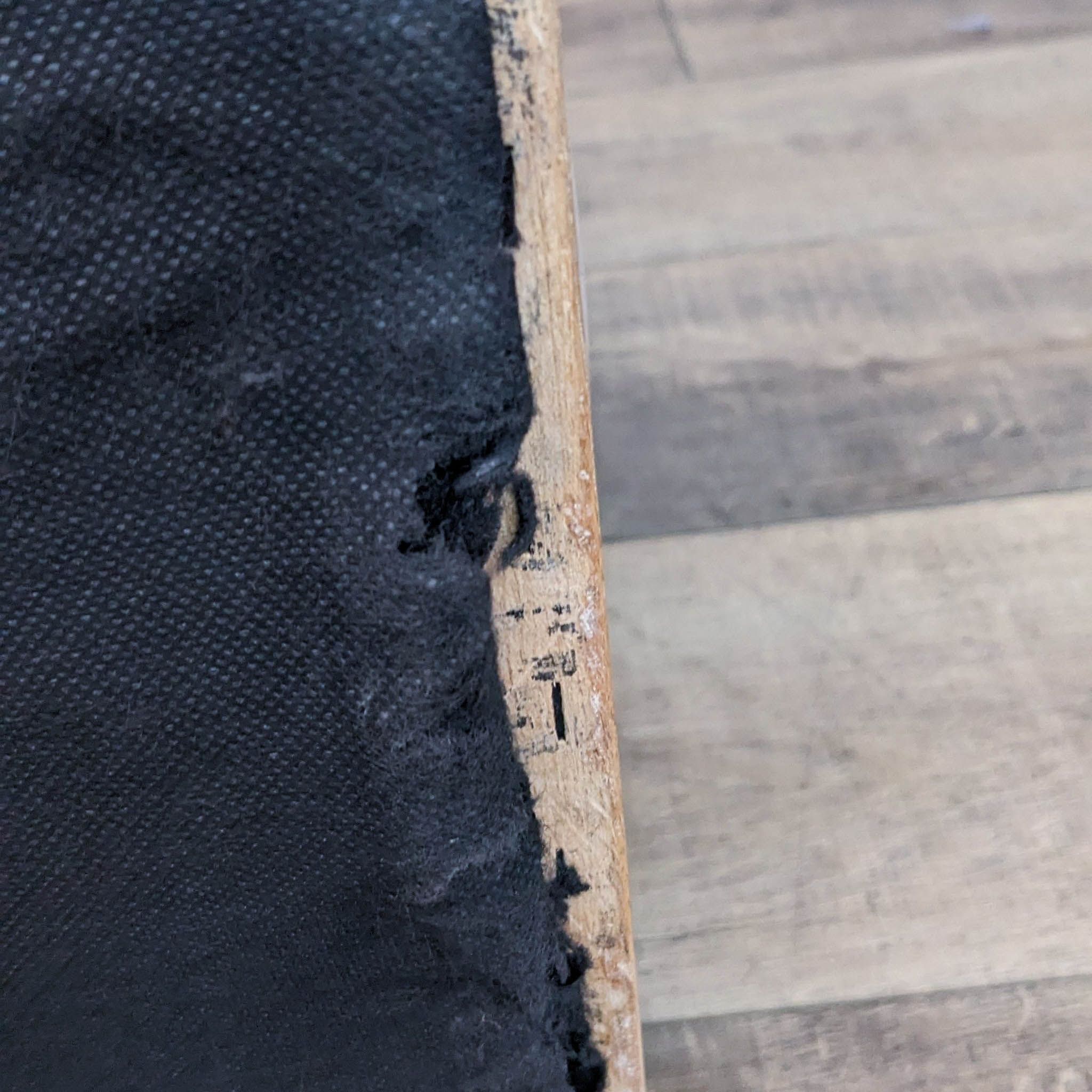 Close-up of the rustic wood frame edge of a Hartland chair with white wash finish, partially upholstered in black microfiber.