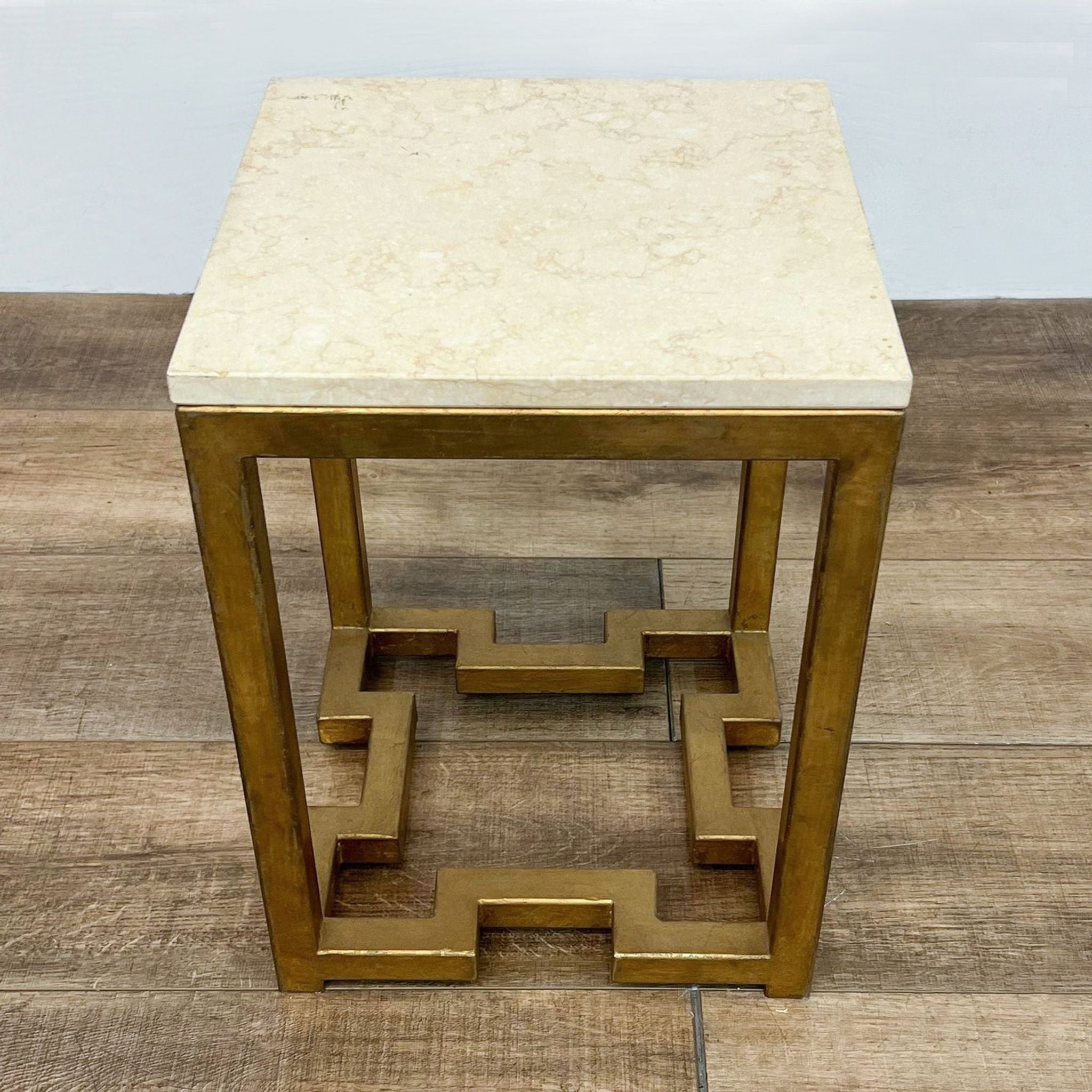 Reperch brand side table with antiqued brass finish metal base and cream-colored top, on a wooden floor.