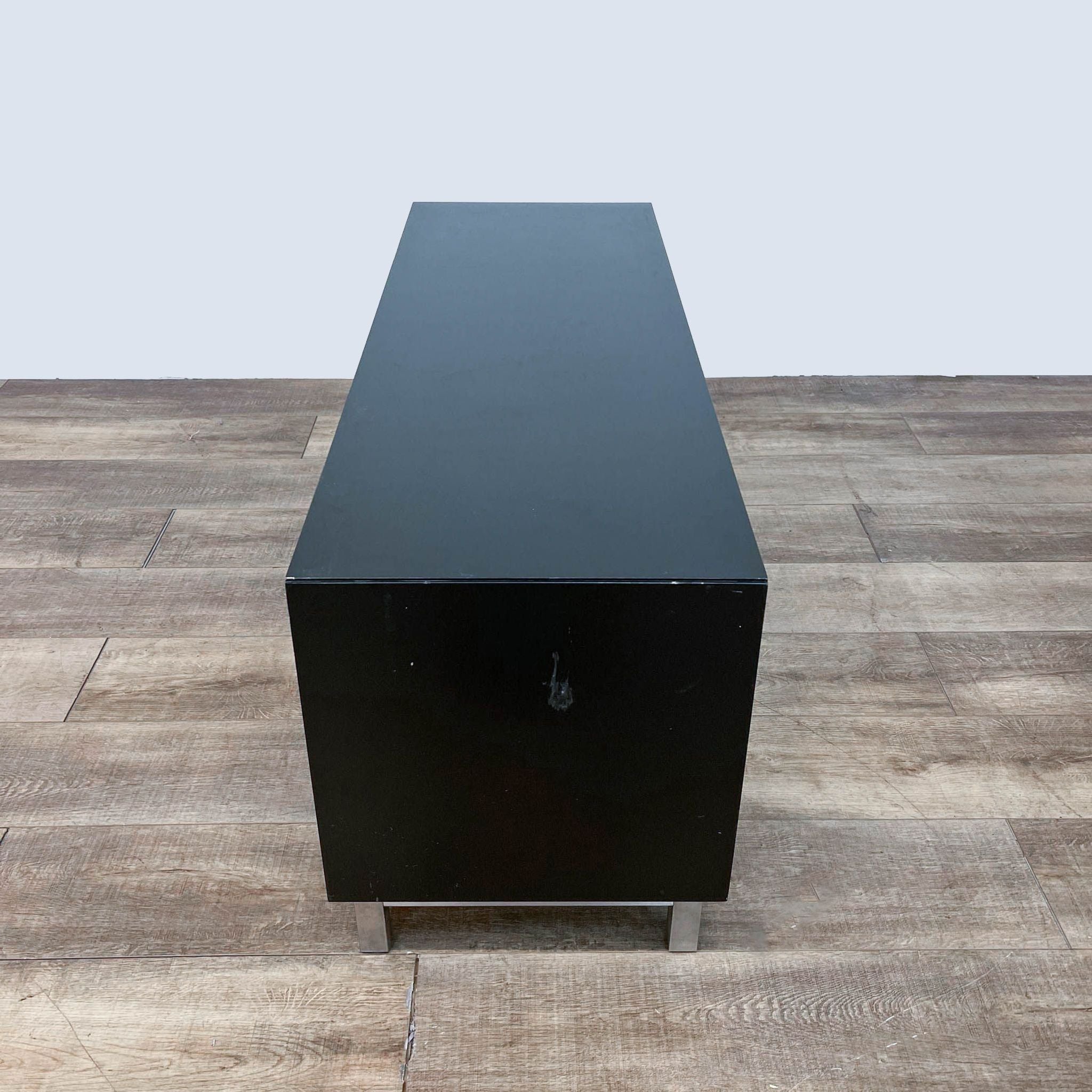 Reperch brand black entertainment center with a chrome base on a wooden floor.