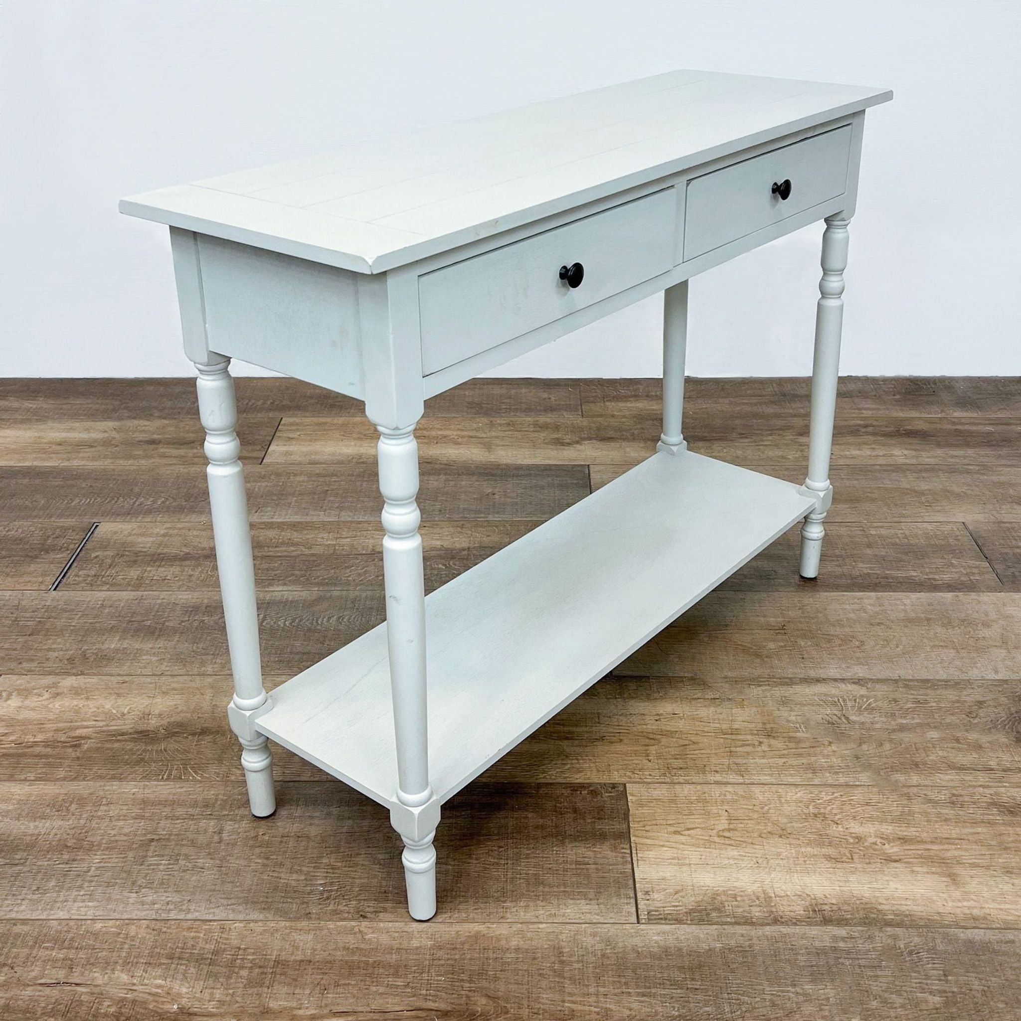 White Reperch wooden console table with two drawers and lower shelf on a wooden floor.