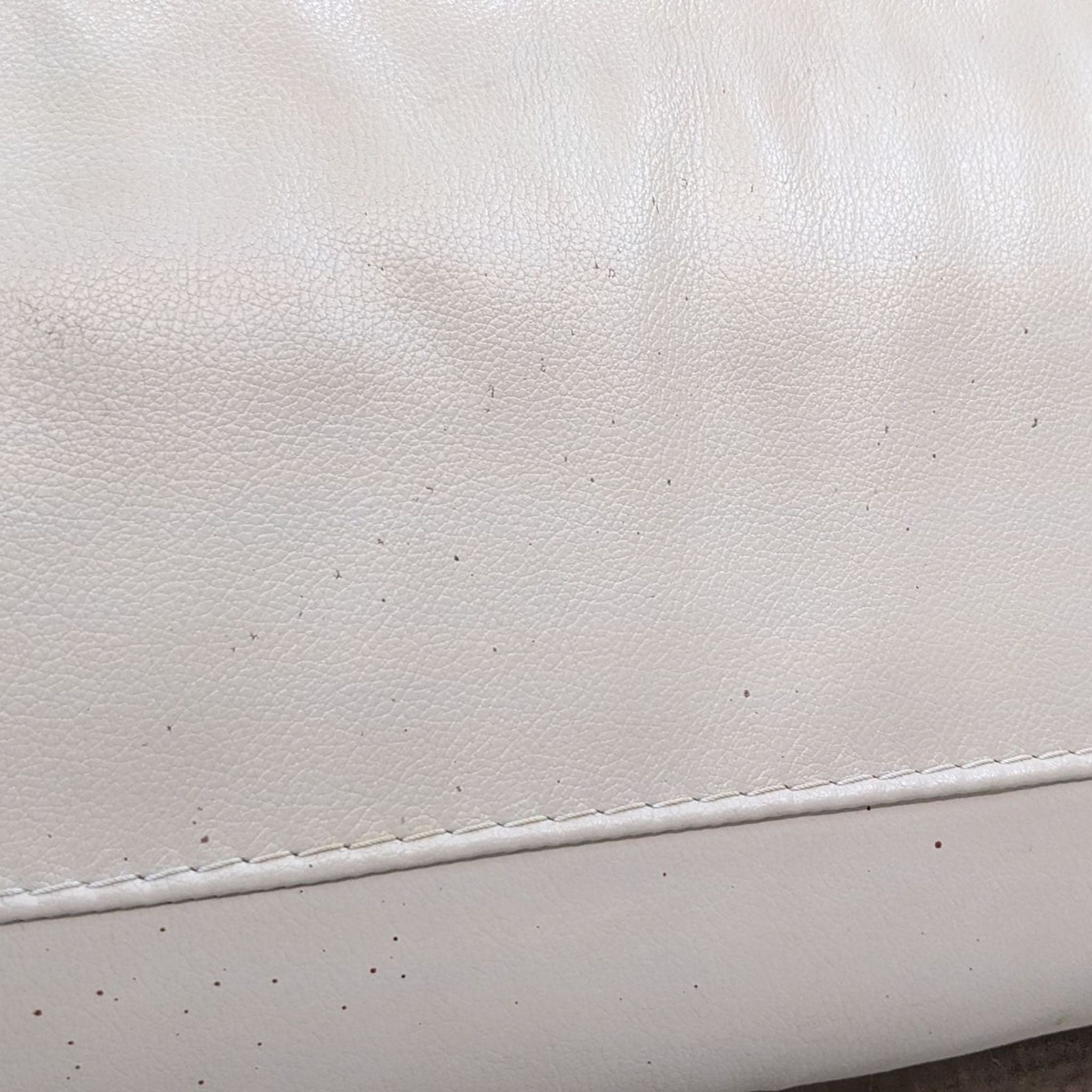 Close-up of a cream-colored tufted leather sofa texture with stitching detail.