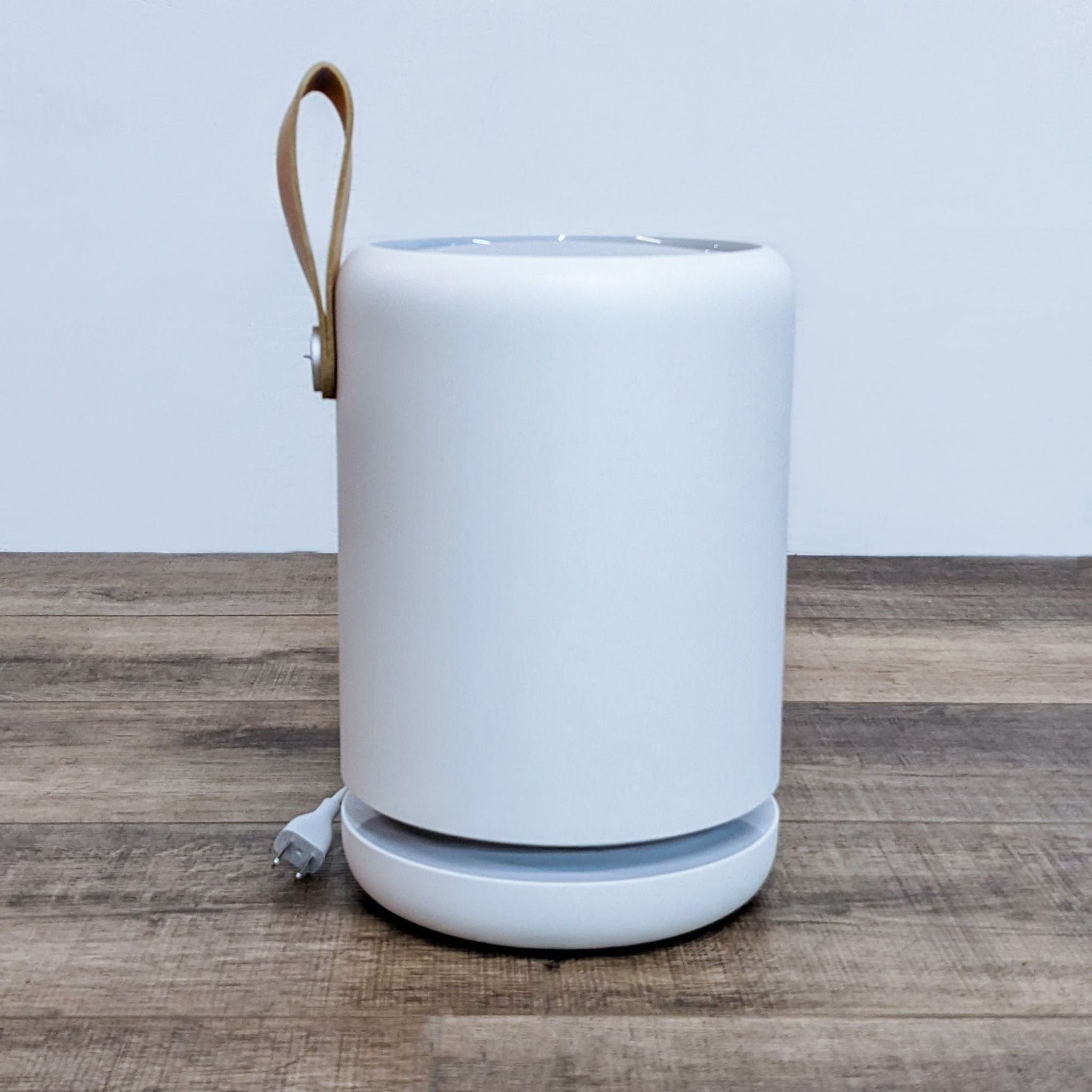Molekule air purifier on wooden floor with a leather handle and a power cord.