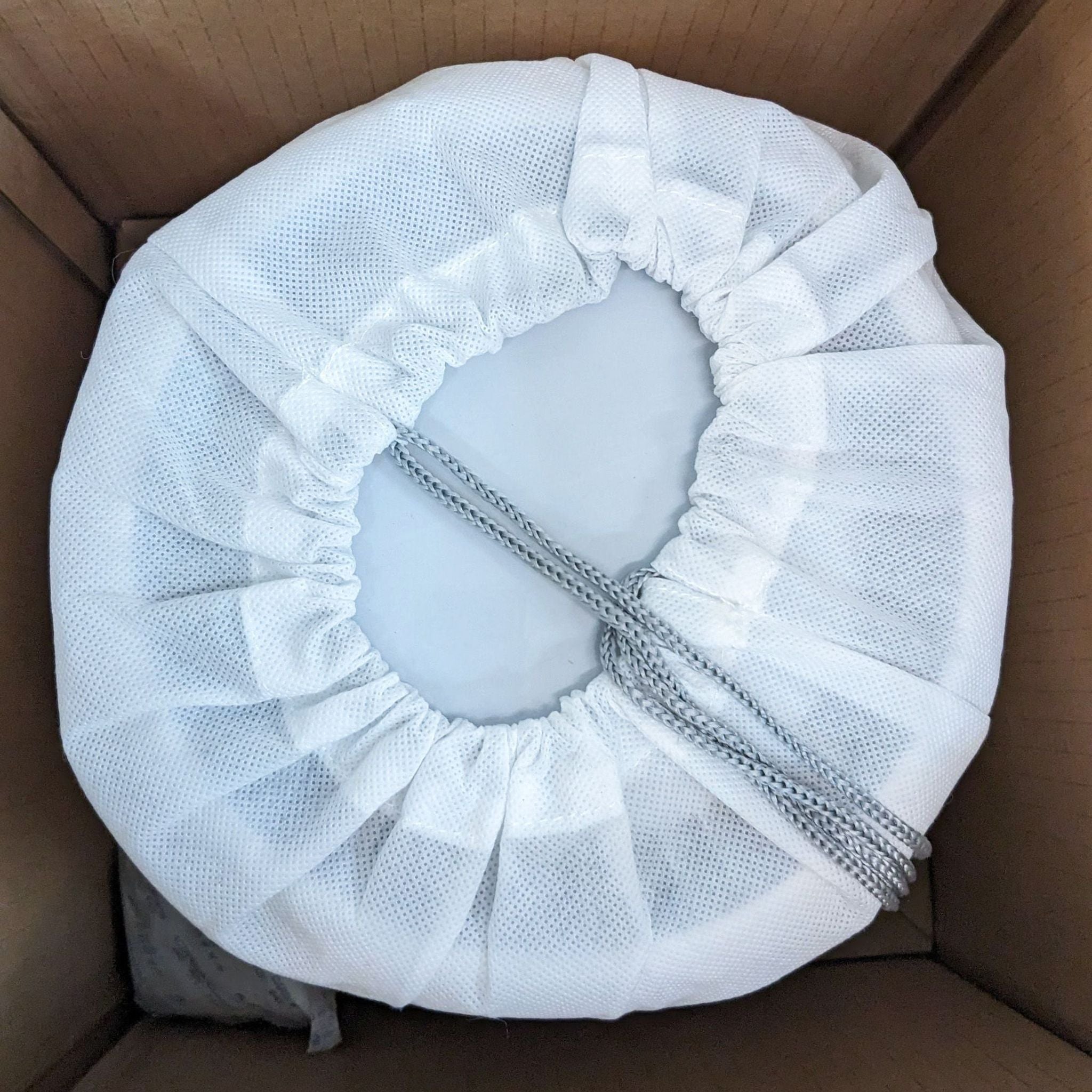 Air purifier pre-filter inside a cardboard box, showing white fabric and elastic edge.