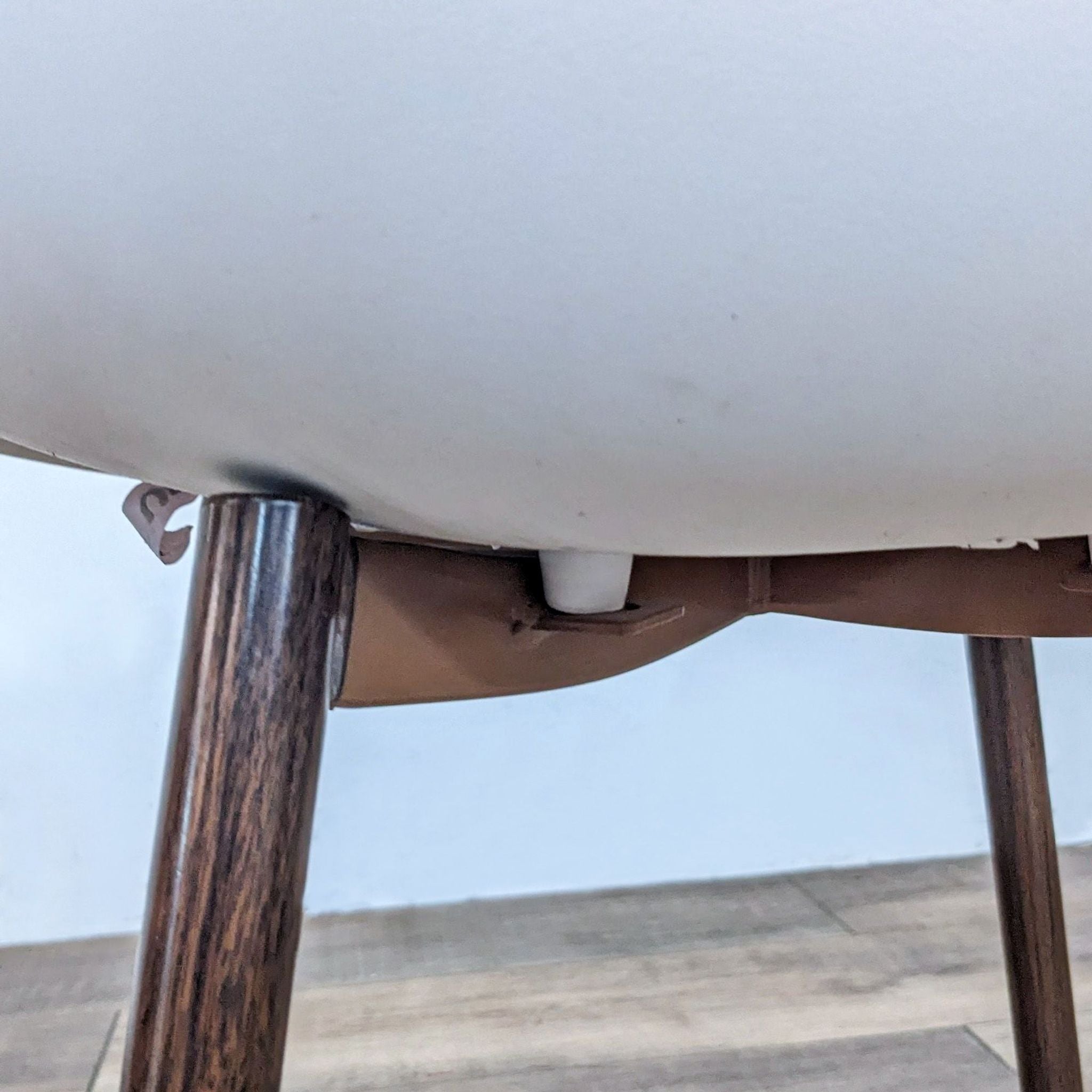 Close-up of the underside of a white Reperch dining chair showing the junction of the molded seat and walnut-finish metal legs.