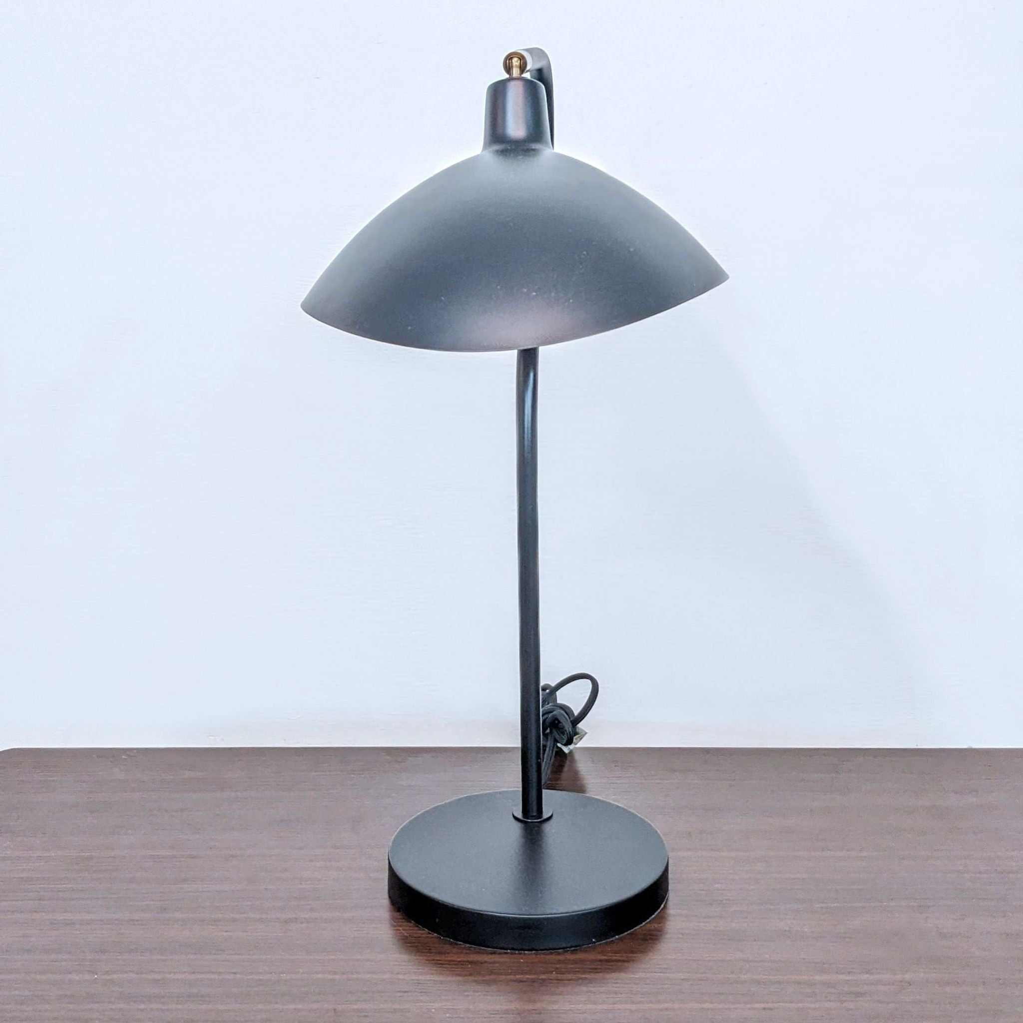 Safavieh brand black desk lamp with a rounded shade and a matte finish, displayed on a wooden table.