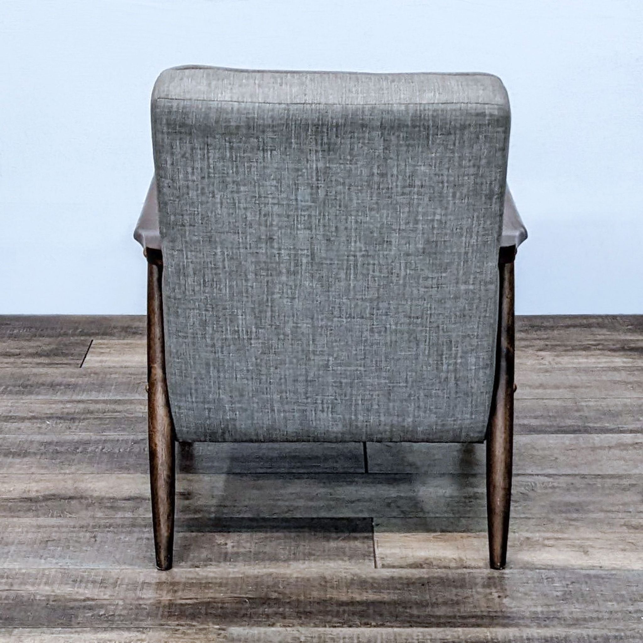 Rear view of Zuo Modern's Rocky armchair featuring a gray woven fabric, button tufting, and angular wooden legs on a wooden floor.