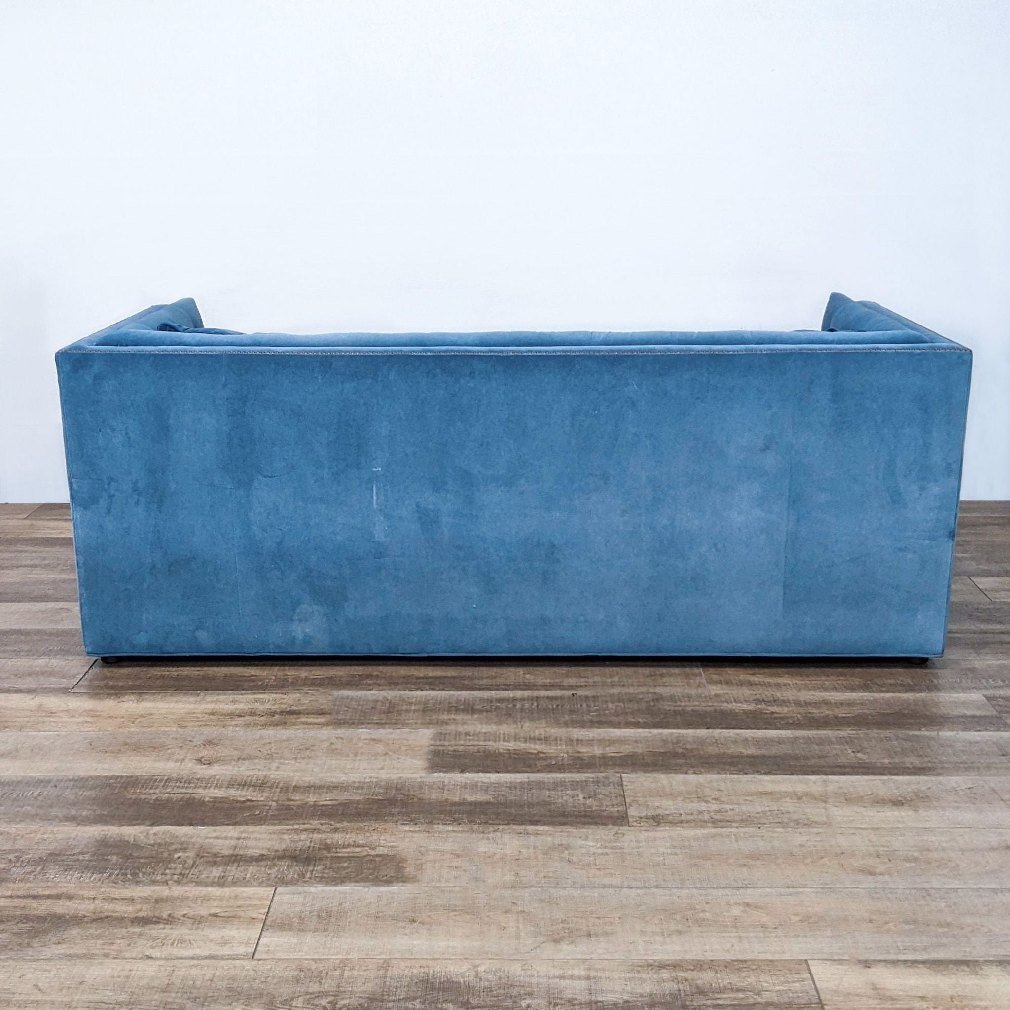 Side view of a blue Bassett 3-seat sofa showcasing its tufted shelter arms and gold nail head trim on a wooden floor.