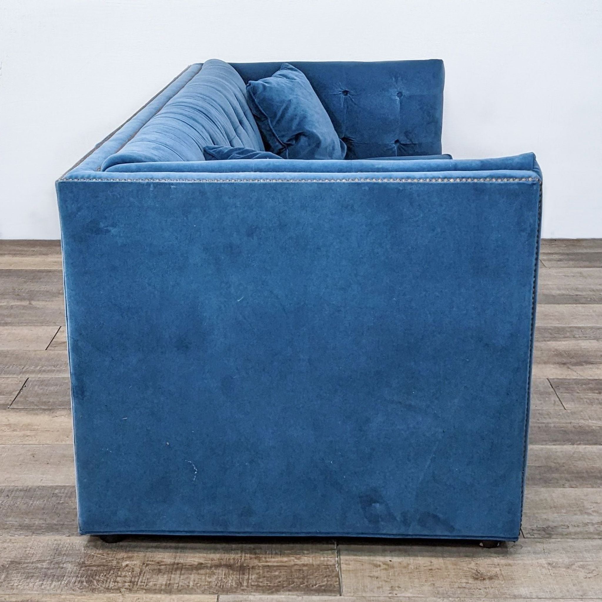 Front-facing view of a blue Bassett 3-seat sofa with tufted design and gold nail head accents on a wood floor.