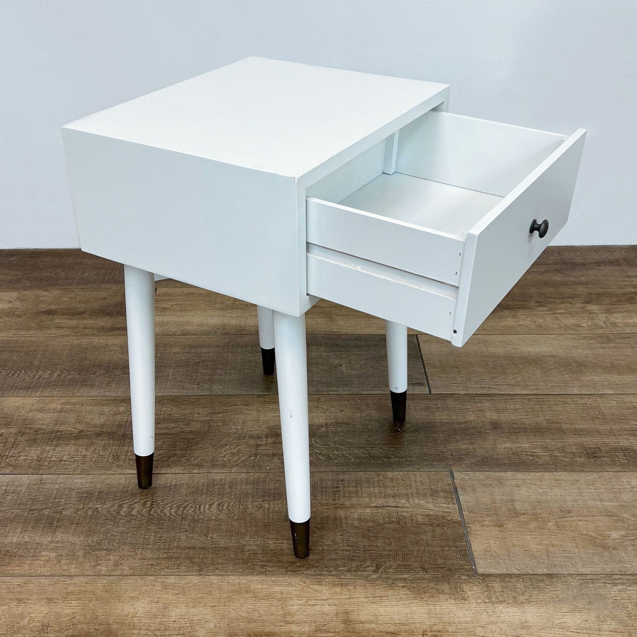 Open drawer on a white Reperch end table revealing storage space, with tipped angle showing legs on wood flooring.