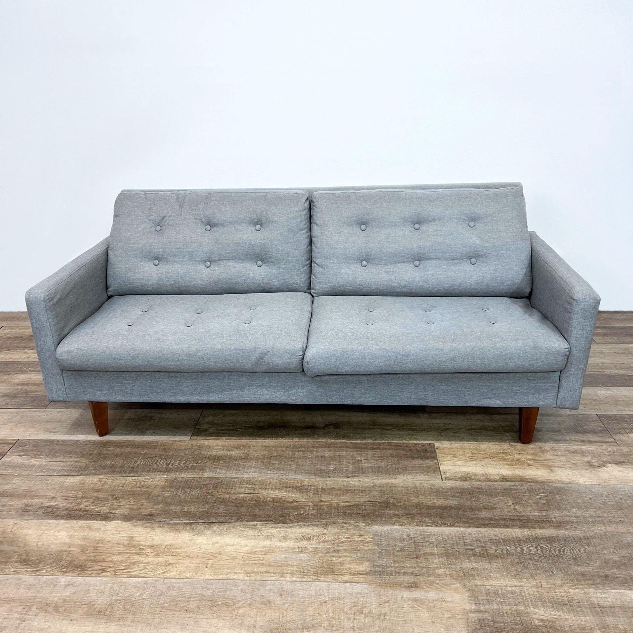 Aeon Furniture 3-seat compact gray tufted sofa with narrow arms and tapered wooden feet on a wood-floor background.