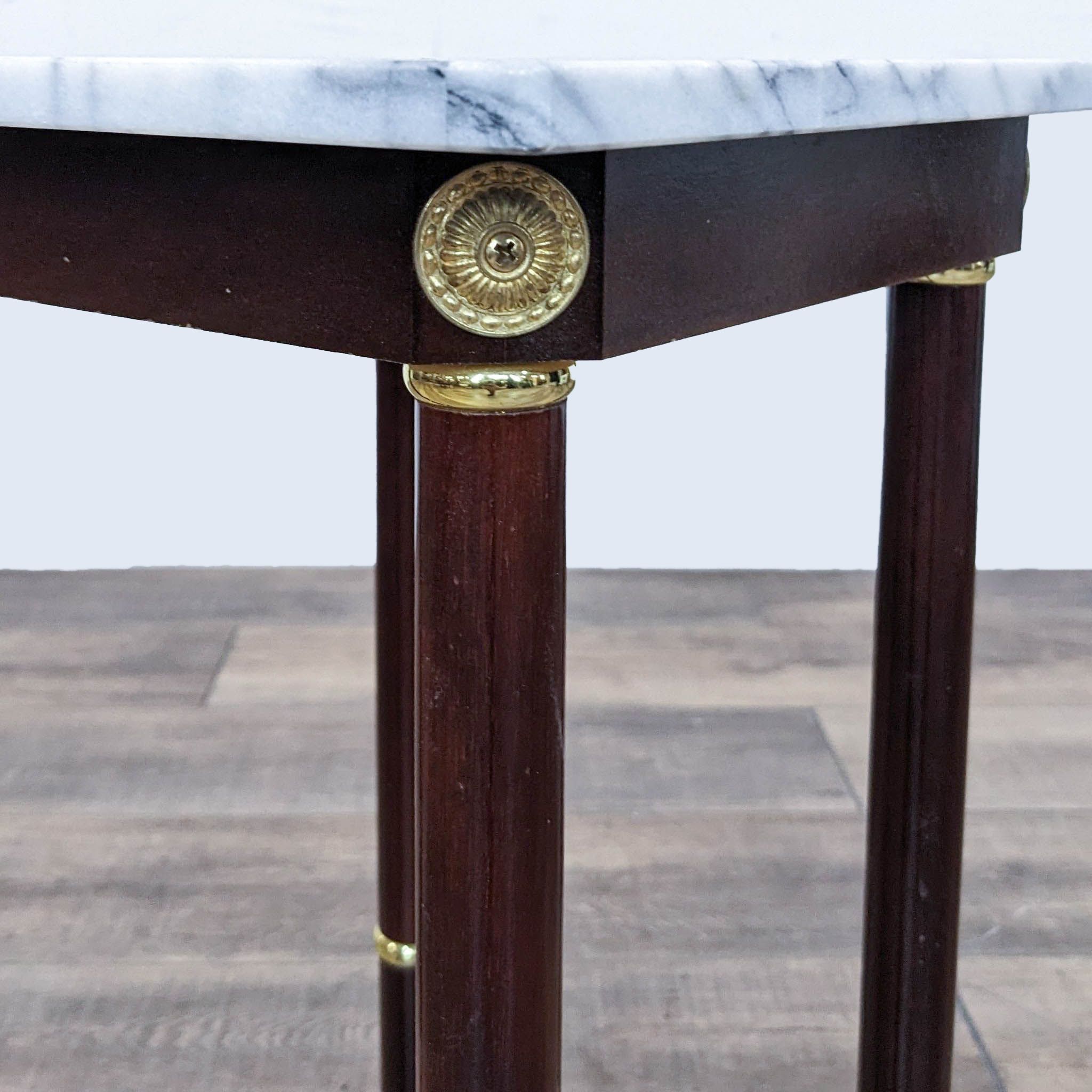 Close-up of Reperch wooden end table leg with brass rings and ornate brass cap, against a marble top.