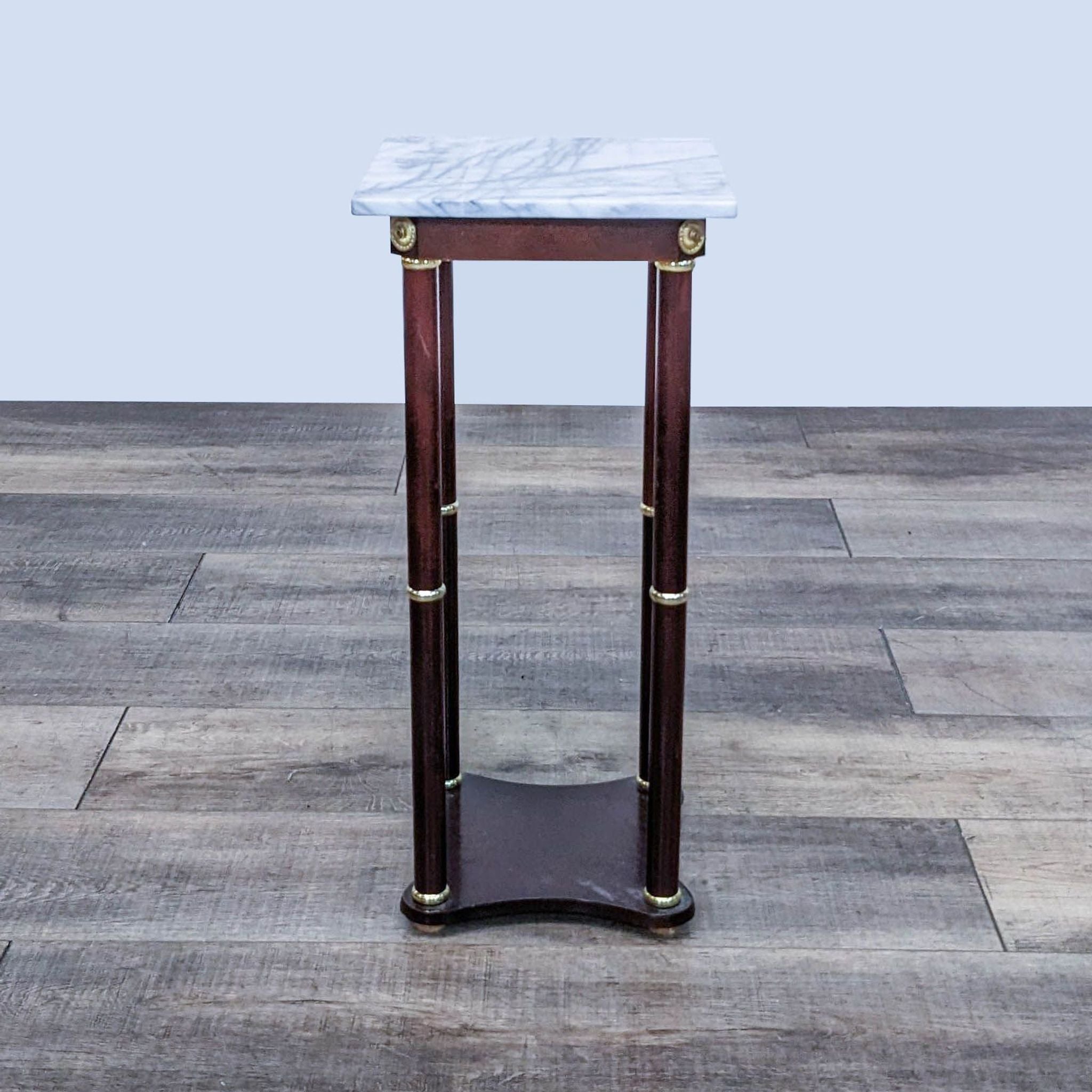 Reperch end table with marble top and wooden legs featuring brass embellishments on a wooden floor.
