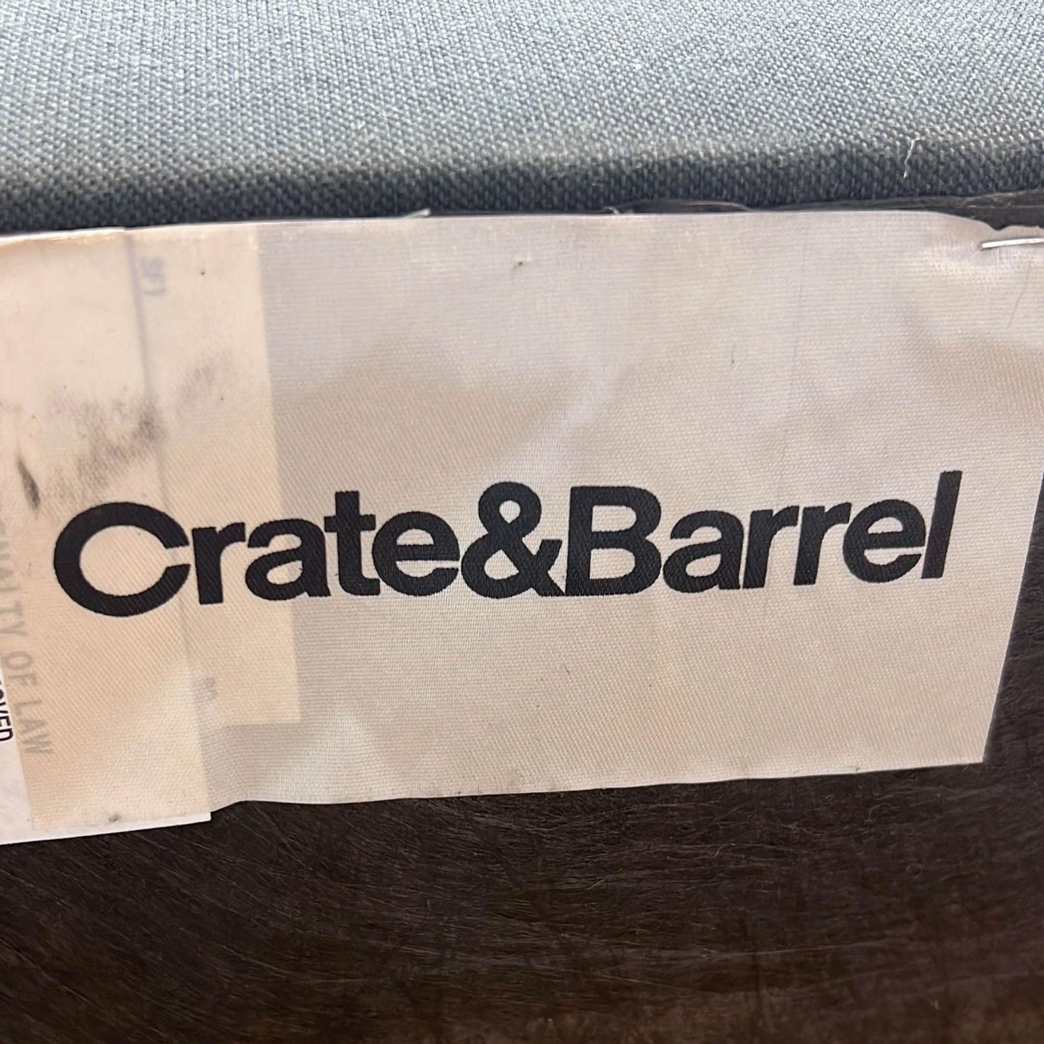 Close-up of Crate & Barrel label on a gray fabric ottoman, reflecting its brand identity.