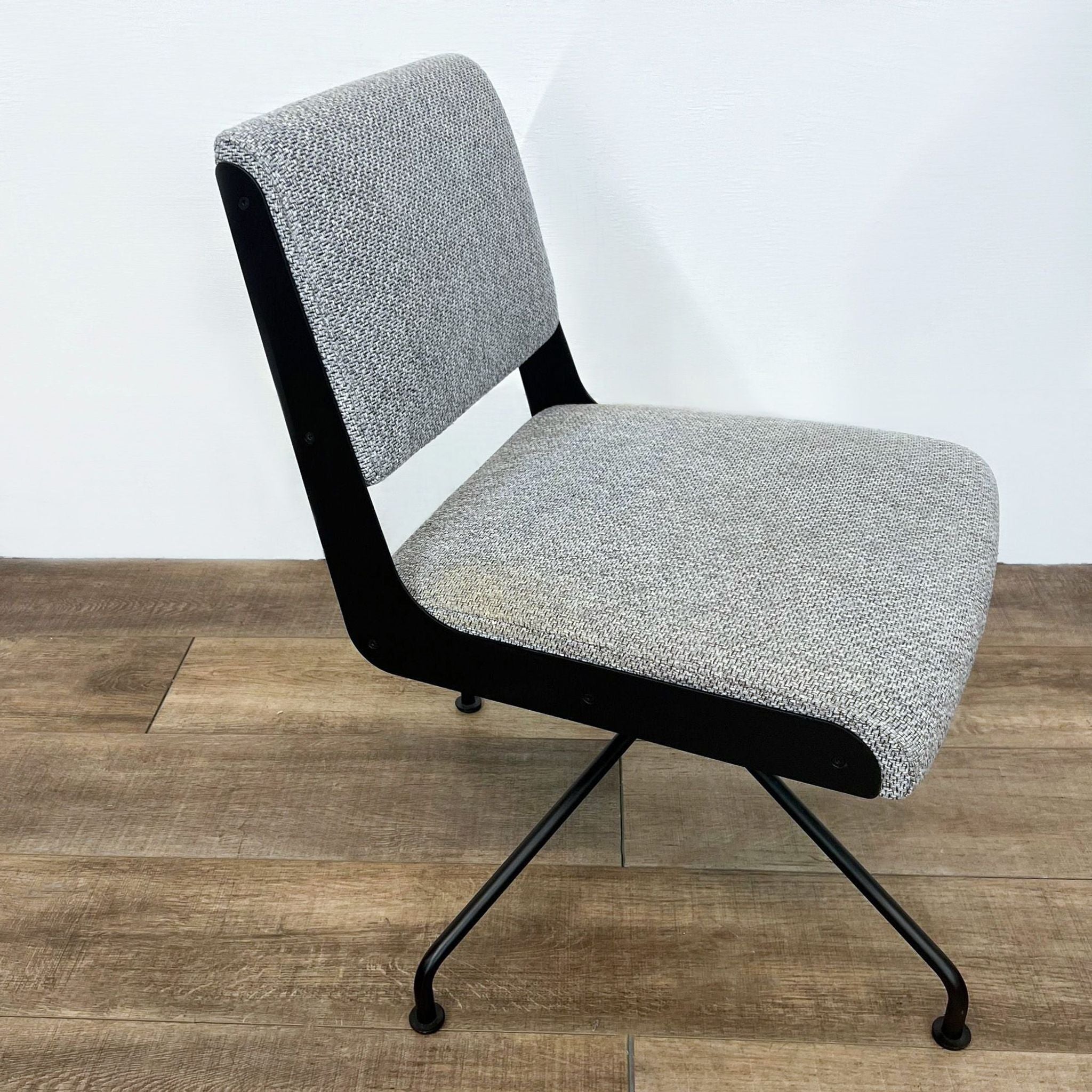 Gray tweed upholstered Rue Cambon chair by CB2, featuring a modern black metal frame and swivel base, against a white wall.