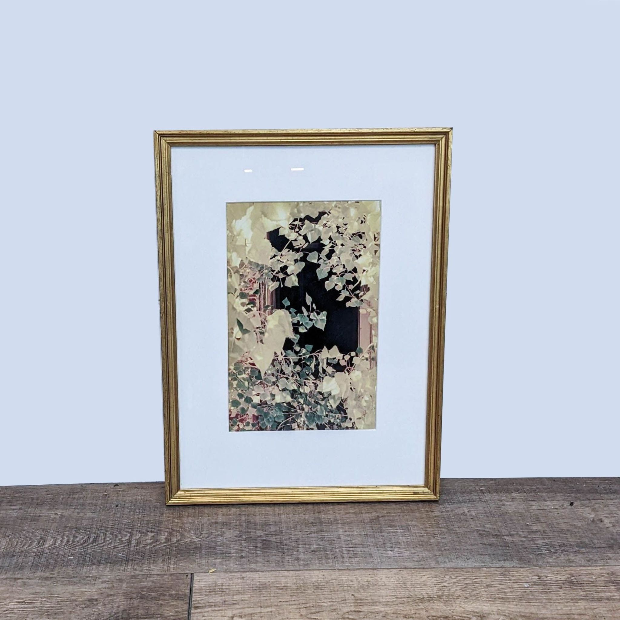 Reperch framed art print featuring tree branches before an open window, in a gold frame on a wooden floor.