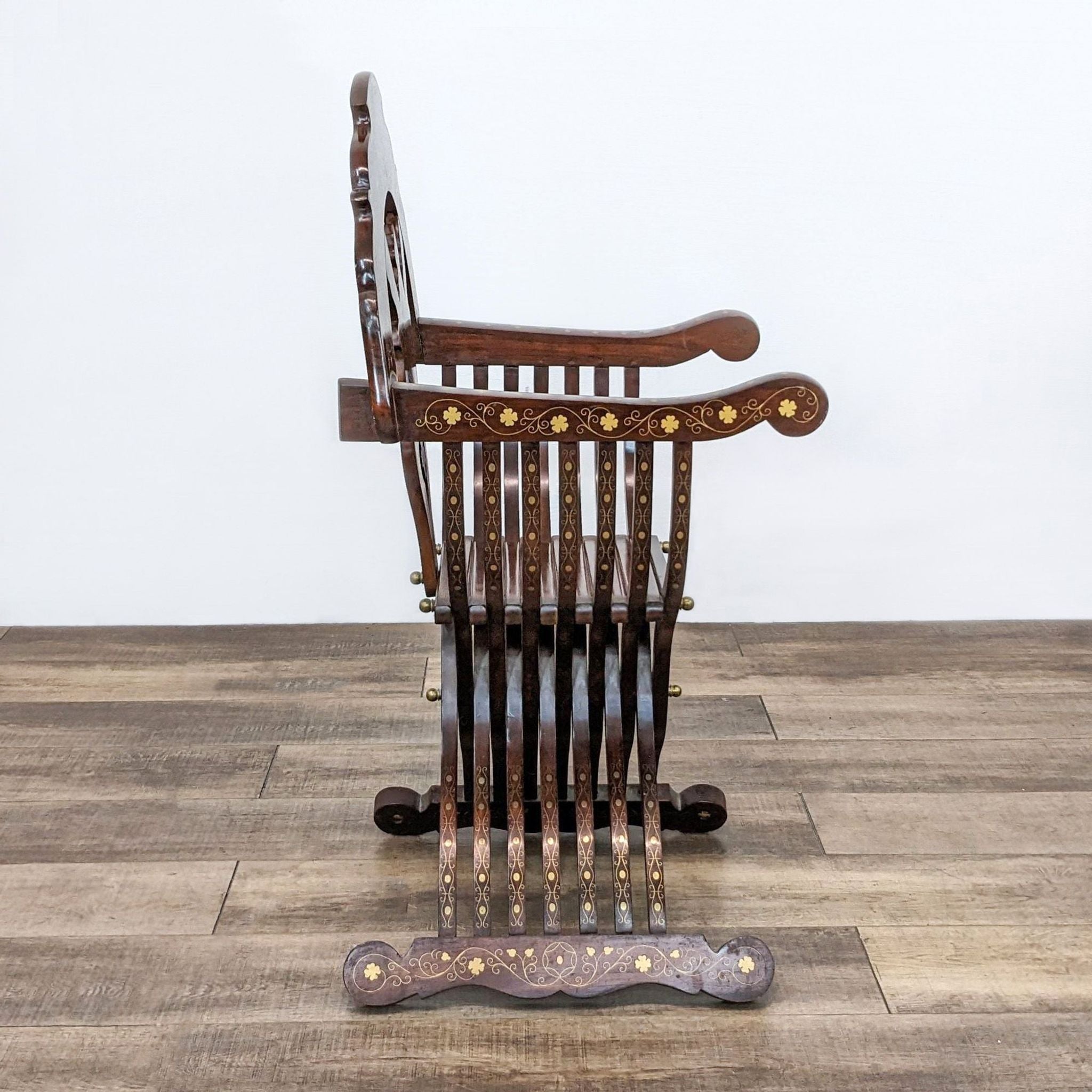 Side perspective of a folded Reperch Savonarola brass inlay chair against a neutral backdrop, emphasizing its compact design.