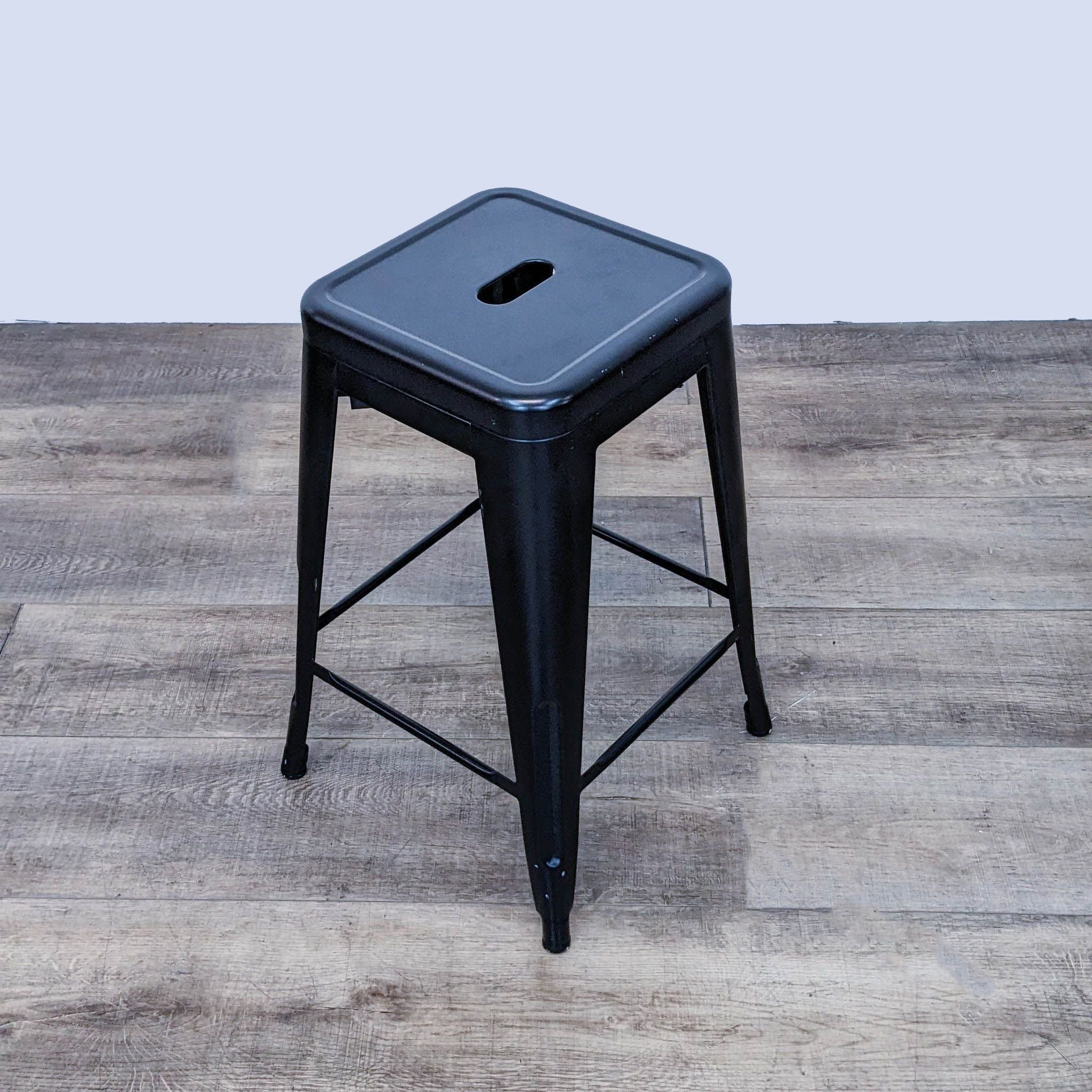 Reperch black metal counter stool with seat hole, angled on wooden floor.