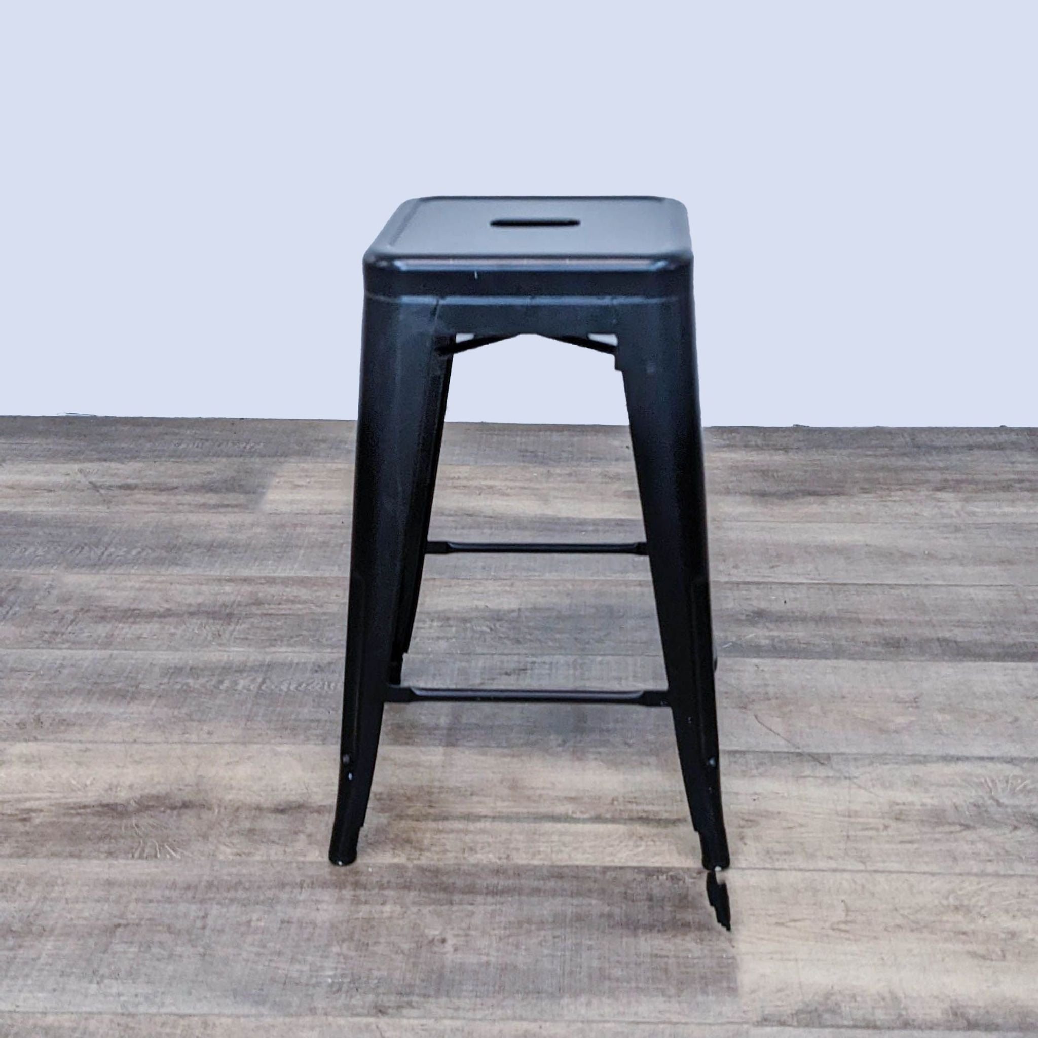 Reperch black metal counter stool with hole seat detailing on wooden floor.